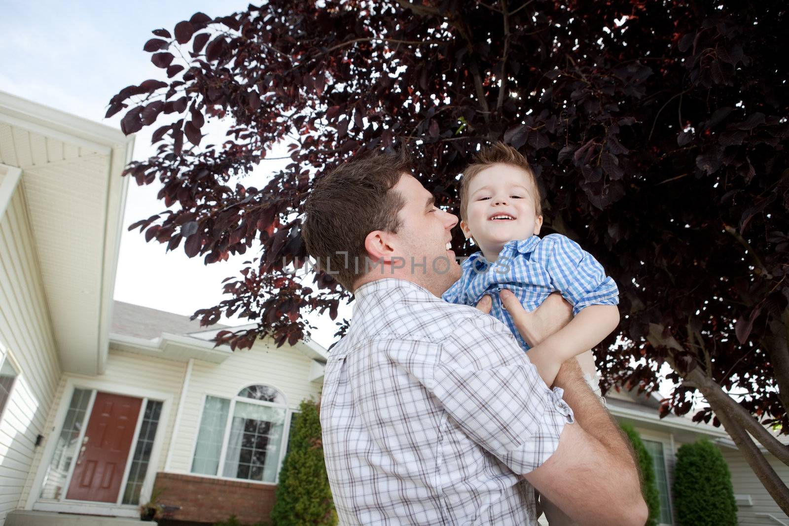 Father Lifting His Little Adorable Boy In Front Of House.