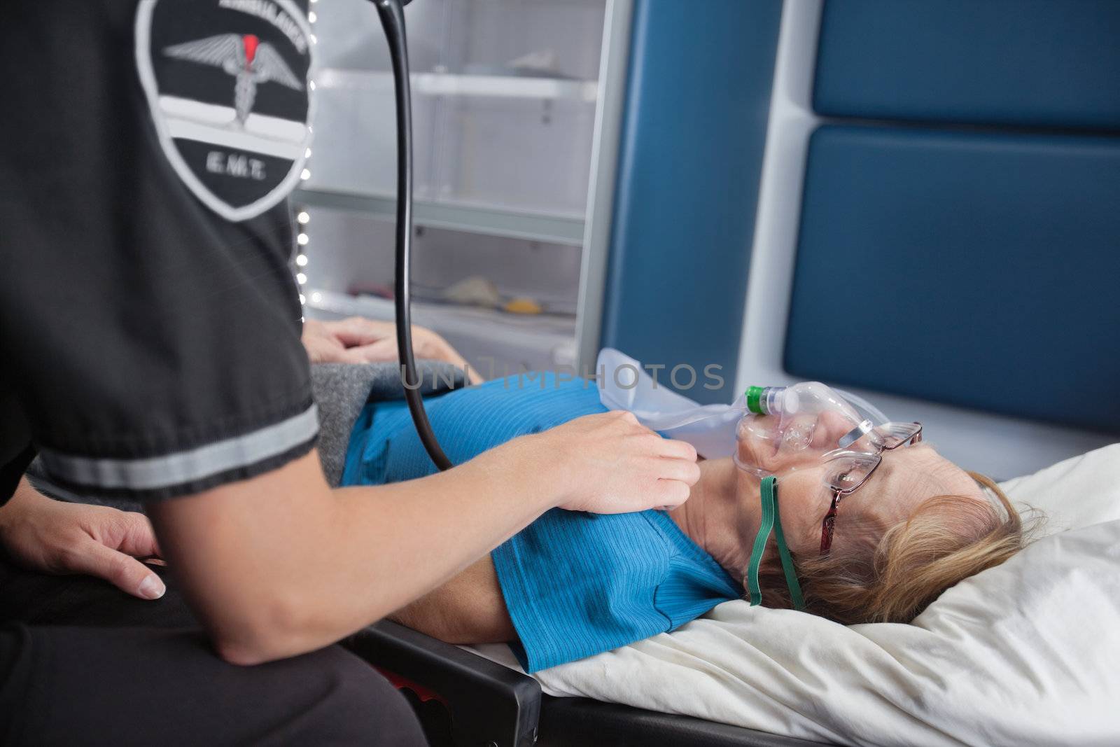 EMT worker listening to pulse of senior woman patient in ambulance