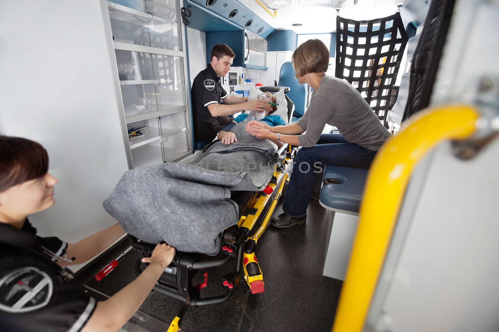 Emergency medical team attending to senior patient in ambulance, caregiver at side