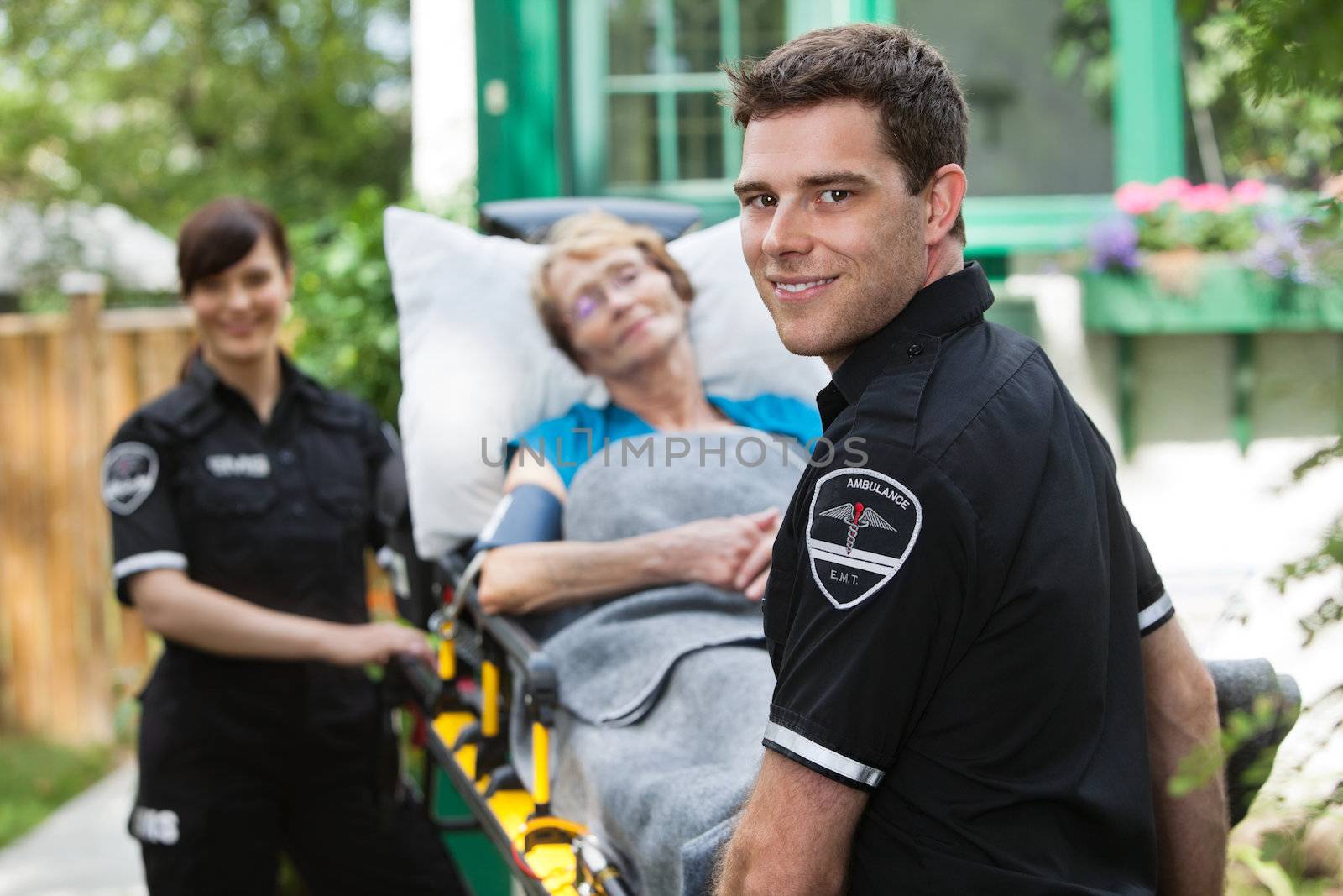 Male ambulance professional with happy senior woman on stretcher