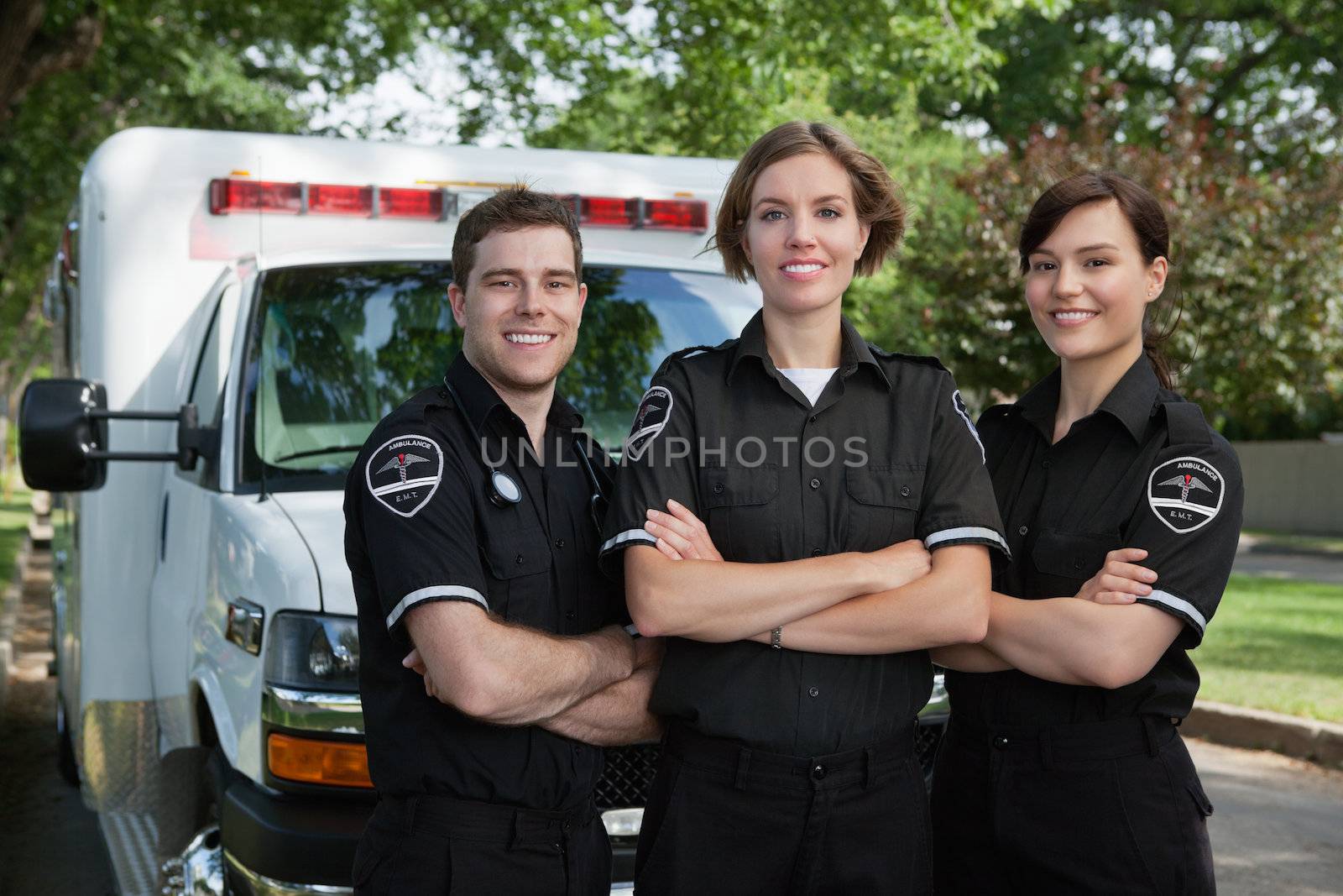 Group of three paramedics standing in front of ambulance with smile