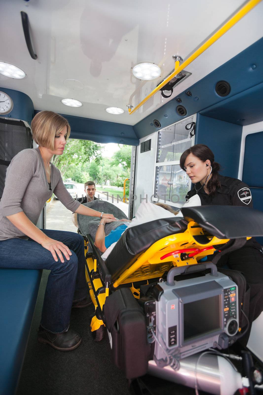 EMT professional caring for a senior woman in an ambulance, caregiver at side
