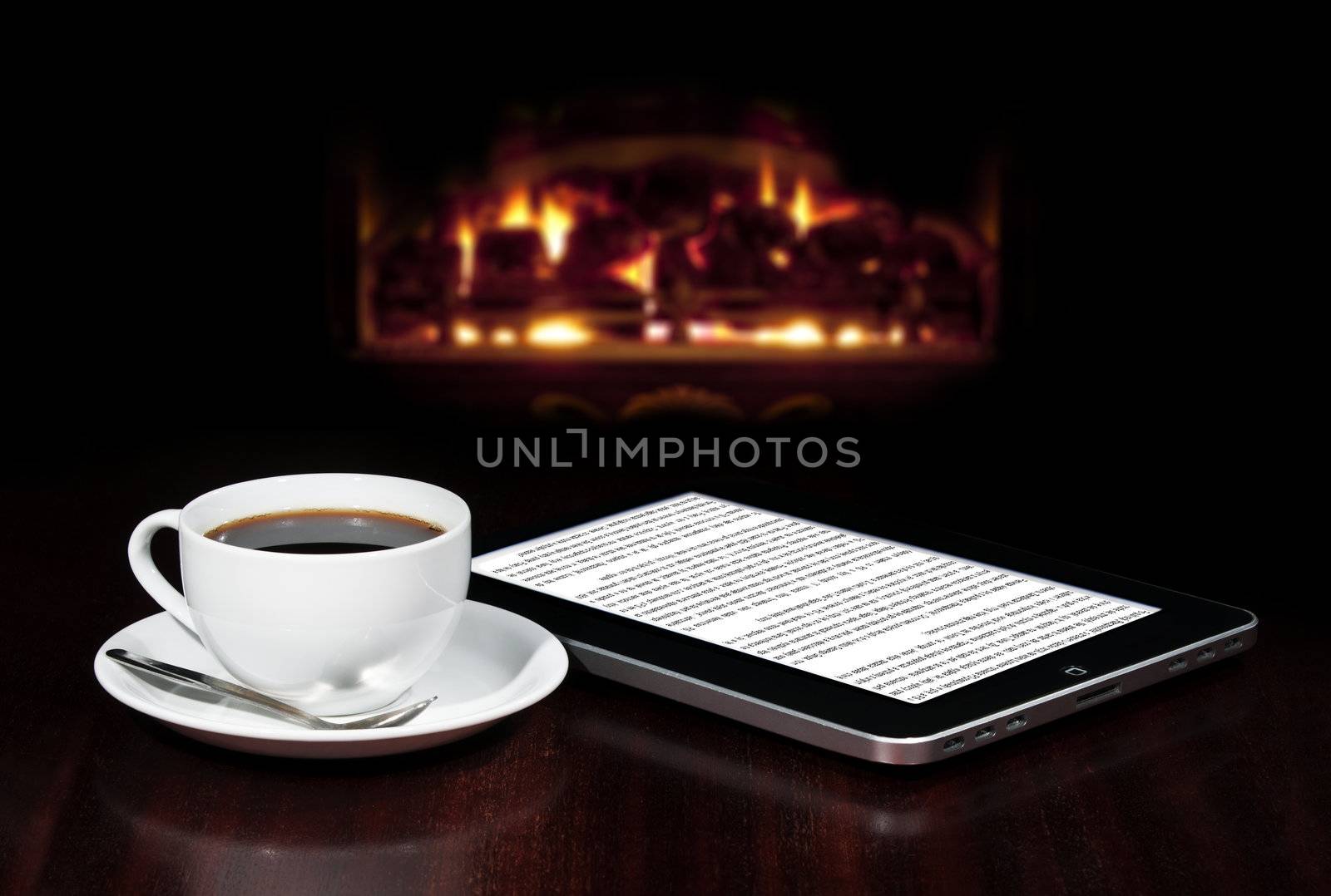 Cap of coffee and tablet on the table top with fireplace in the background.