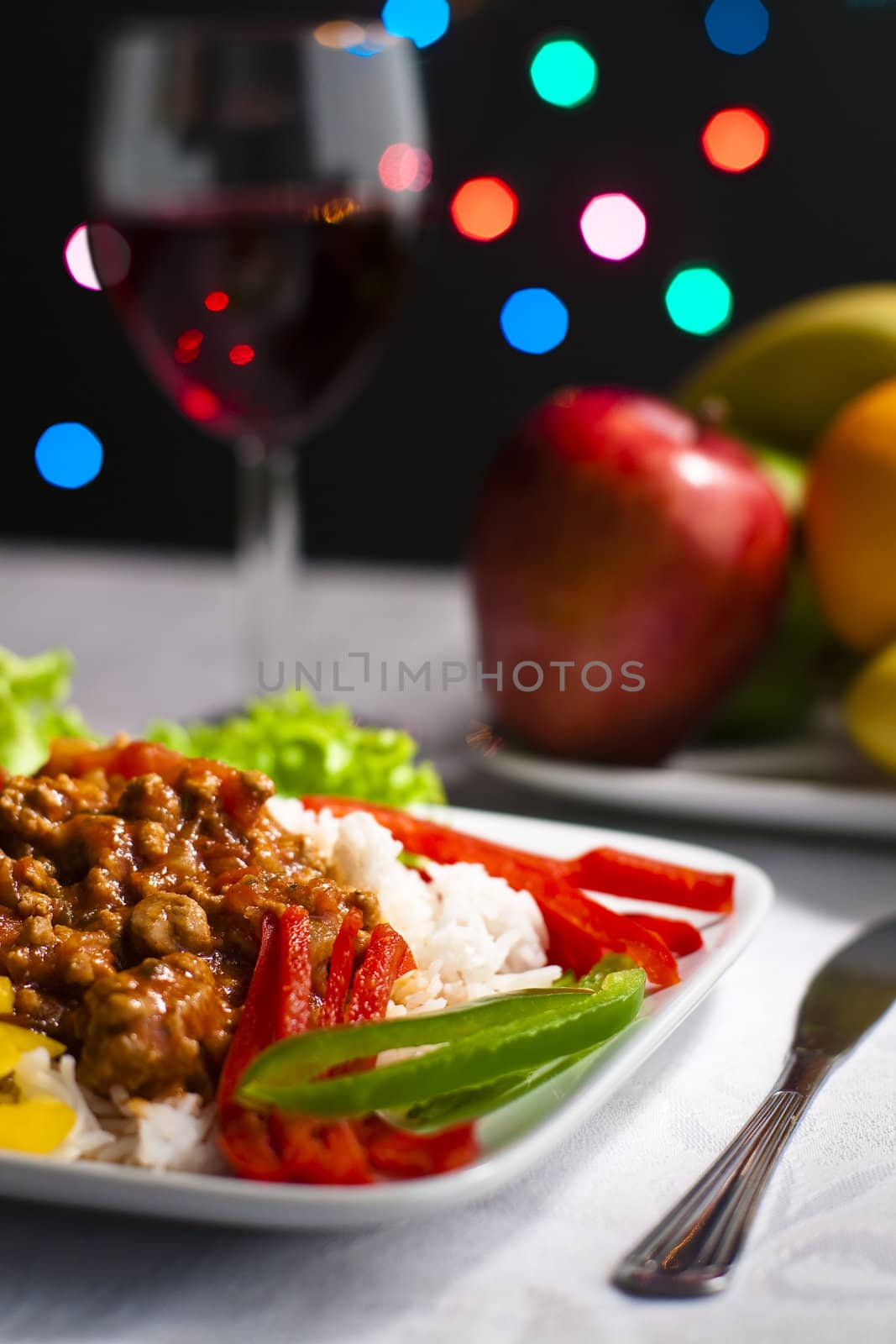 Dinner on tabletop with wine, fruits and bokeh lights in background.