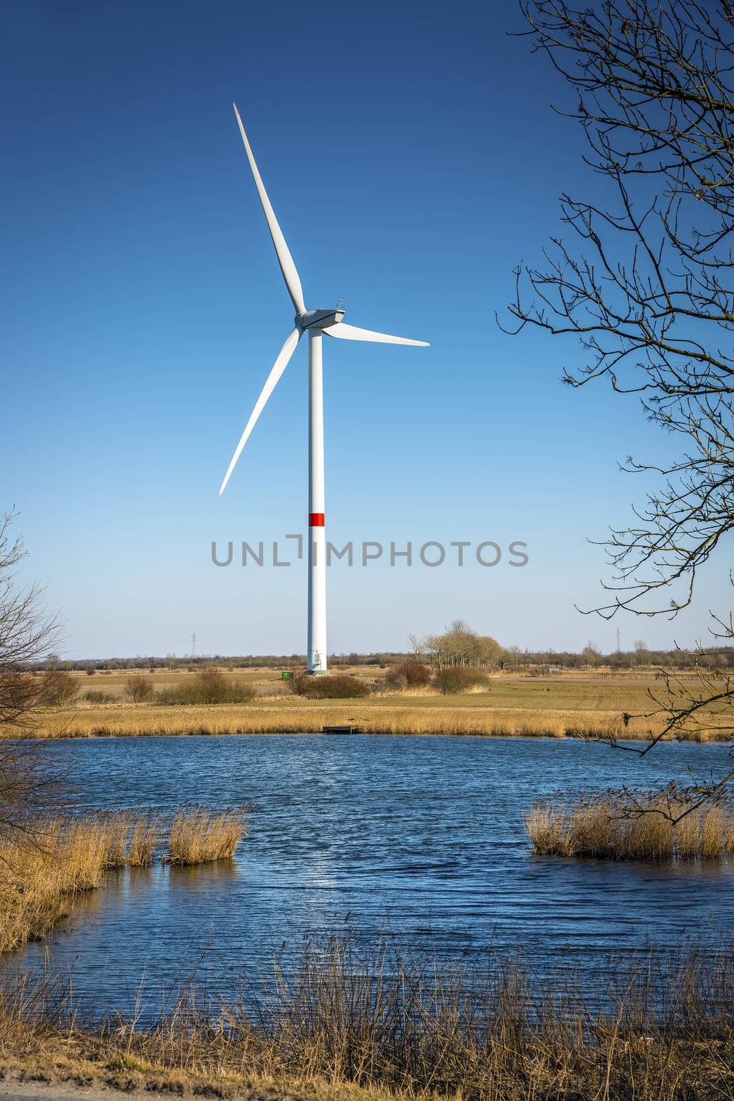 Windmill in a landscape with grass, trees and lake on a sunny day.