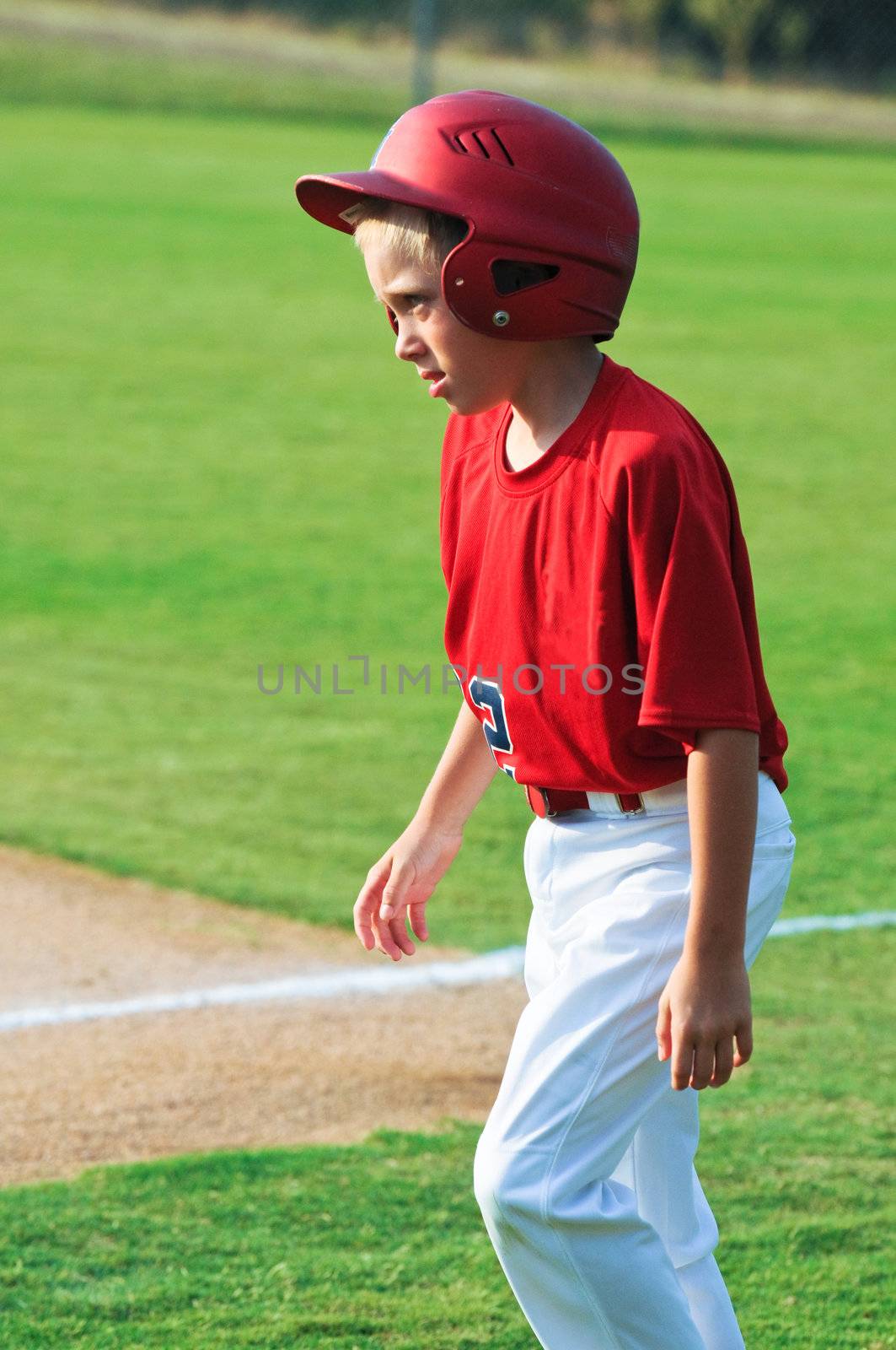 Little league youth baseball boy with helmet walking across ballpark.