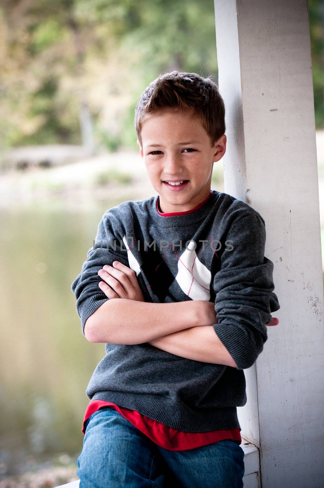 A cute young boy posing next to a pole in front of a pond.