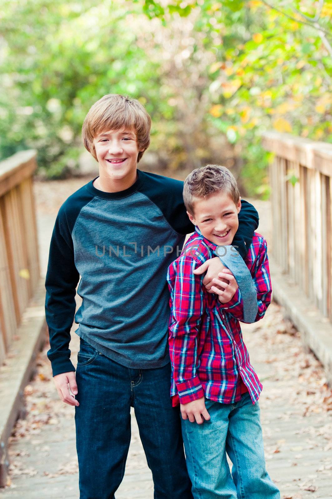 Portrait of brothers with older boy tickling younger boy on a bridge outdoors.