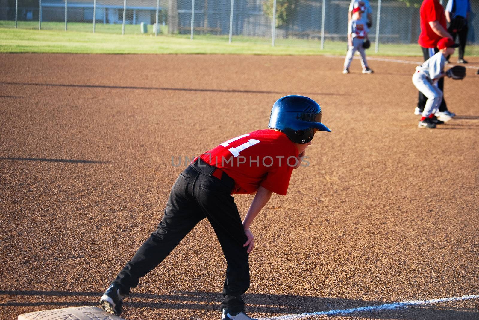 Youth baseball player on third base getting ready to run.