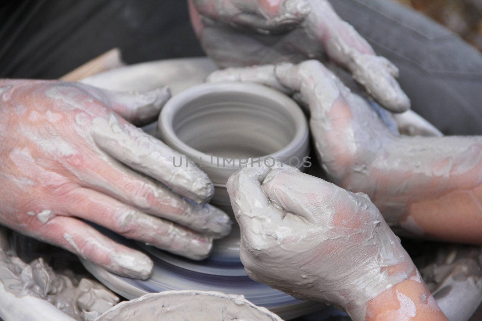 A potters hands guiding a child hands to help him to work with the ceramic wheel