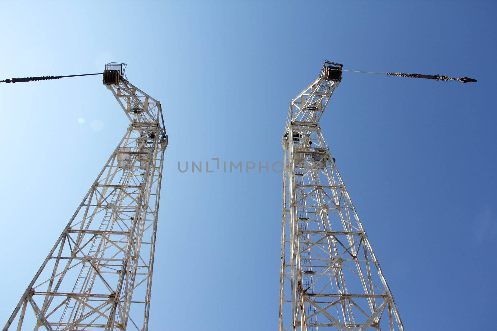 Two high cranes on blue clear sky background