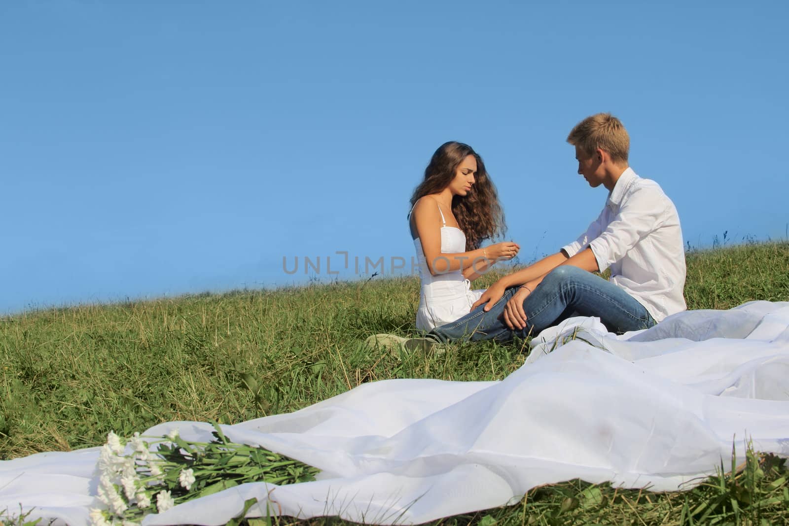 Young couple sitting on summer field discussing something and smiling