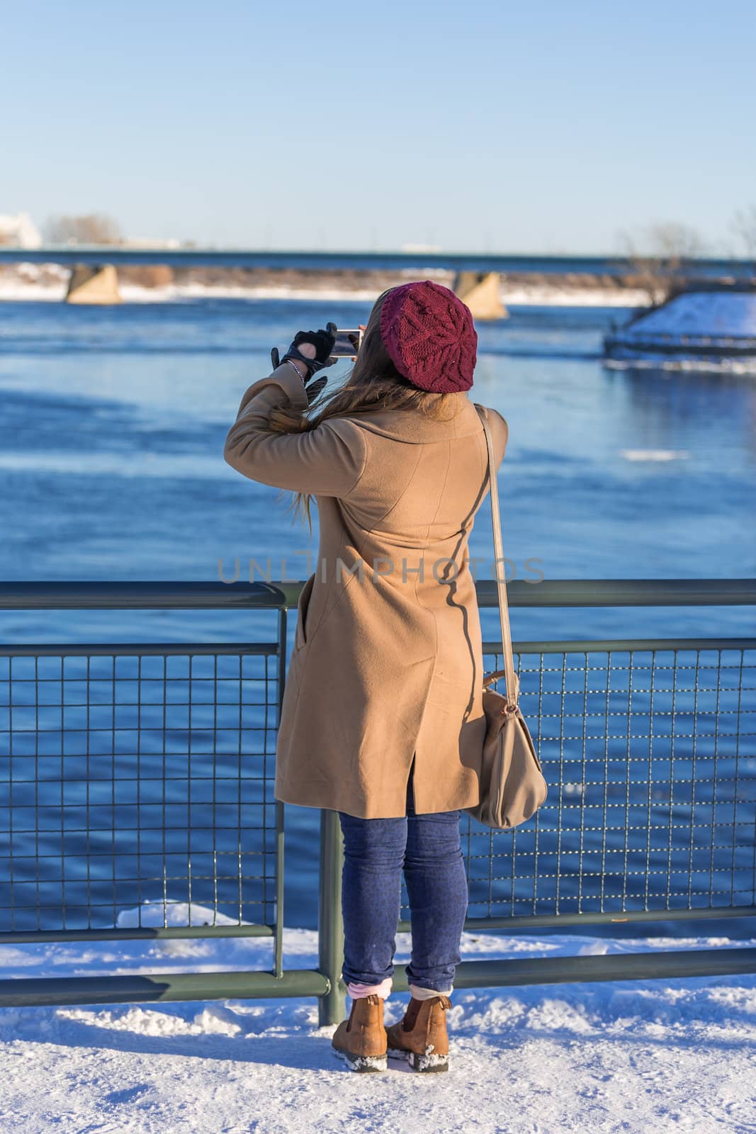 A random woman taking a picture of Saint Lawrence river in cold winter day in Montreal, Quebec, Montreal