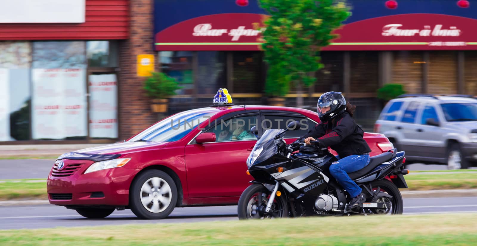 Red taxi no hands driving and a susuki motorcycle driving side by side in Taschereau street, Brossard, Quebec, Canada