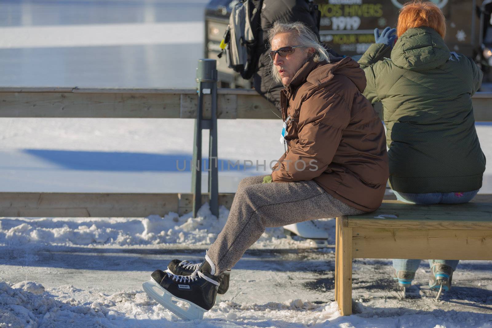 A man is taking a break after a hard ice skating session, by sitting, relaxed, on a cold bench in the Skating Rink in Old Port of Montreal, Quebec ,Canada