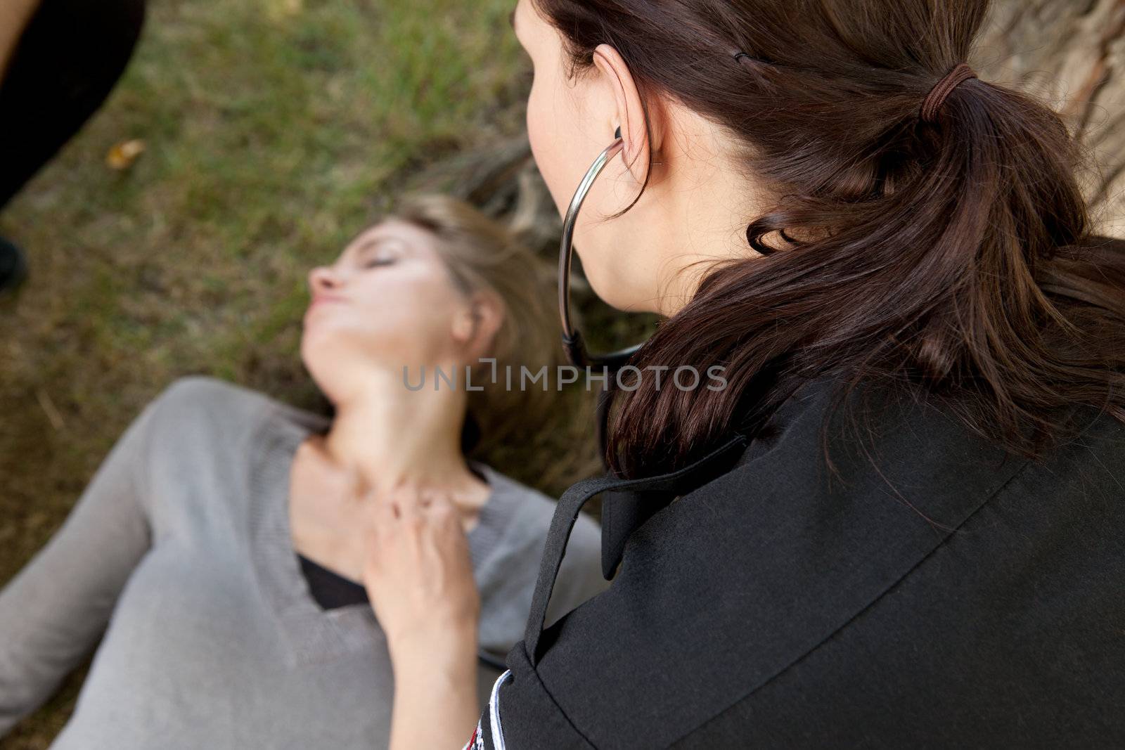 Paramedic checking vitals on an injured woman in a park.  Shallow depth of field, focus on paramedic