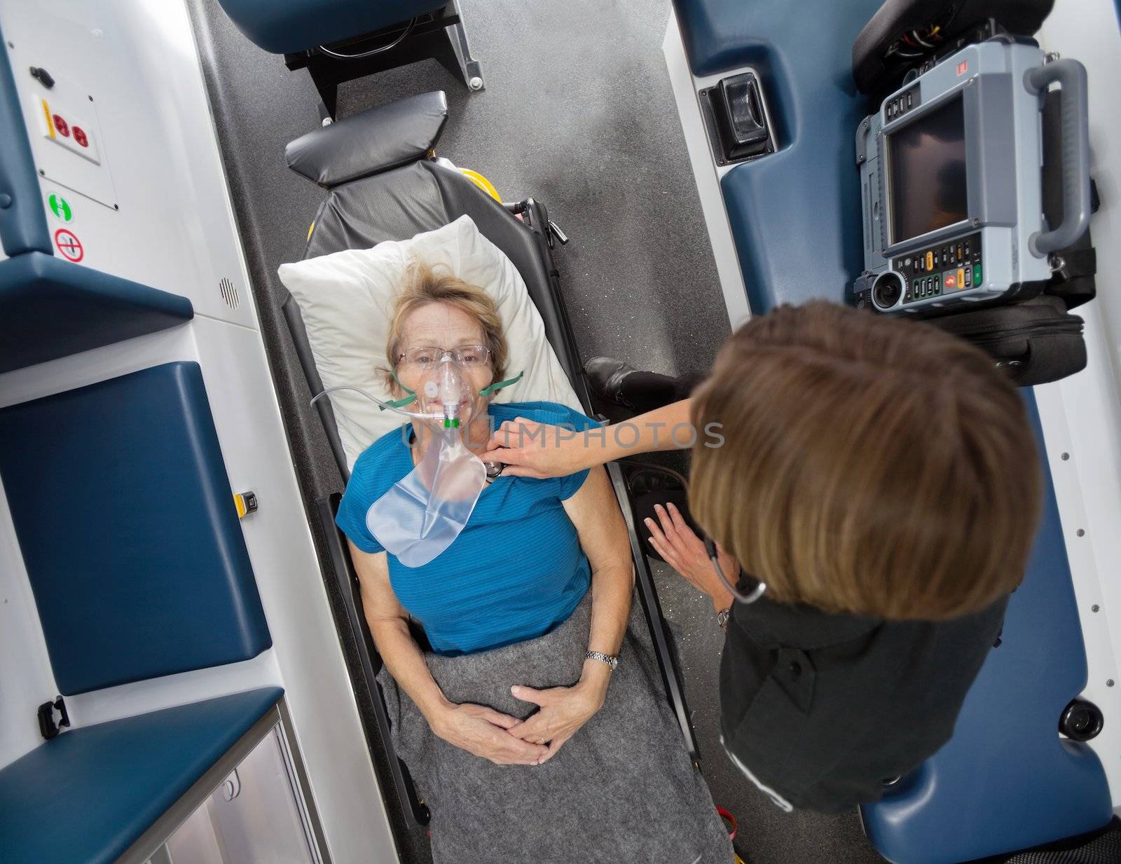 Overhead view of senior woman patient in ambulance receiving oxygen and having heart rate measured