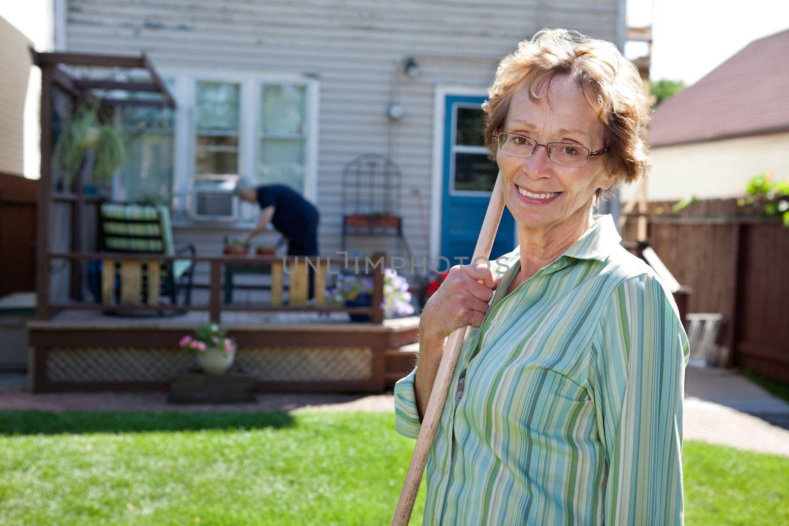 Portrait of elderly woman holding gardening tool with friend in the background