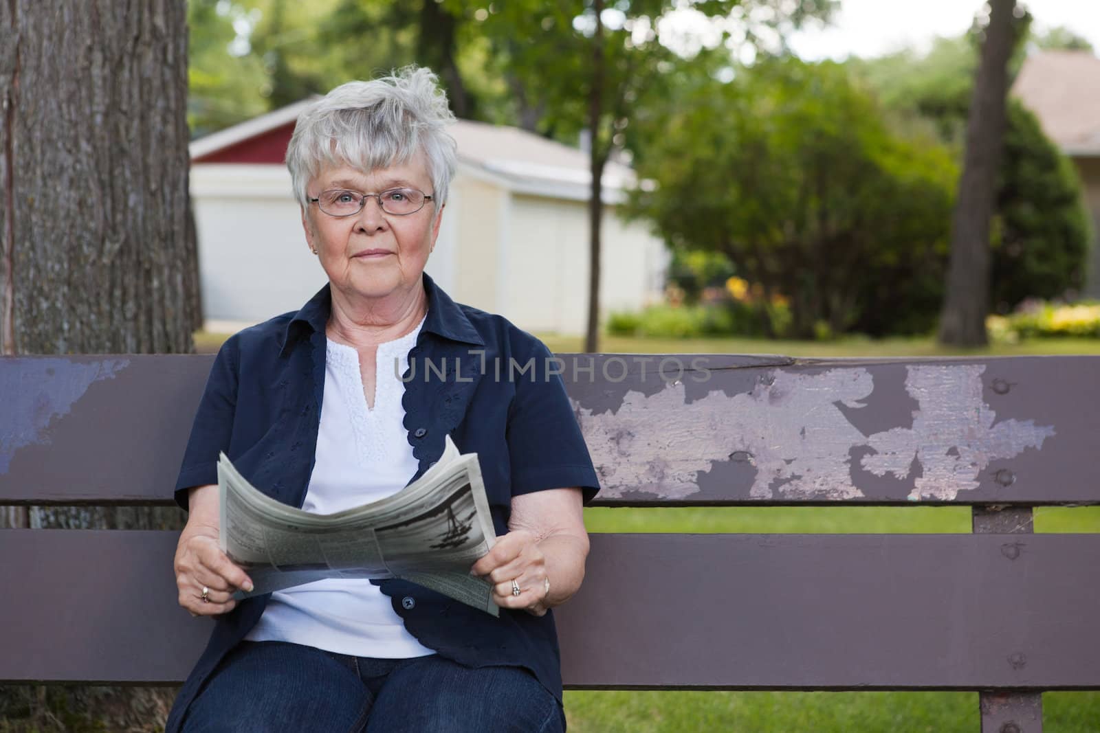 Portrait of senior woman holding newspaper, sitting on park bench