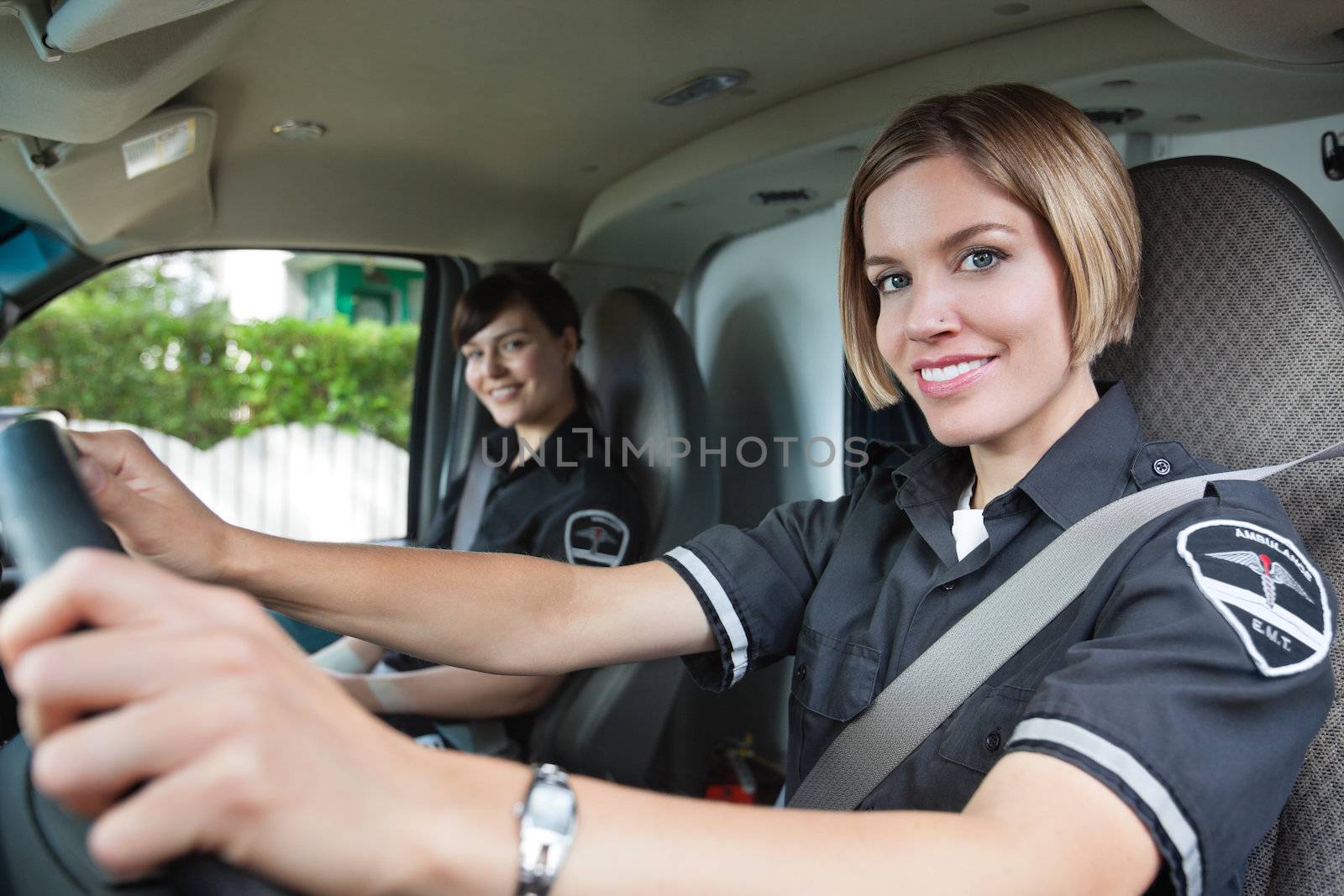 Portrait of happy female paramedic driving ambulance with team member in background