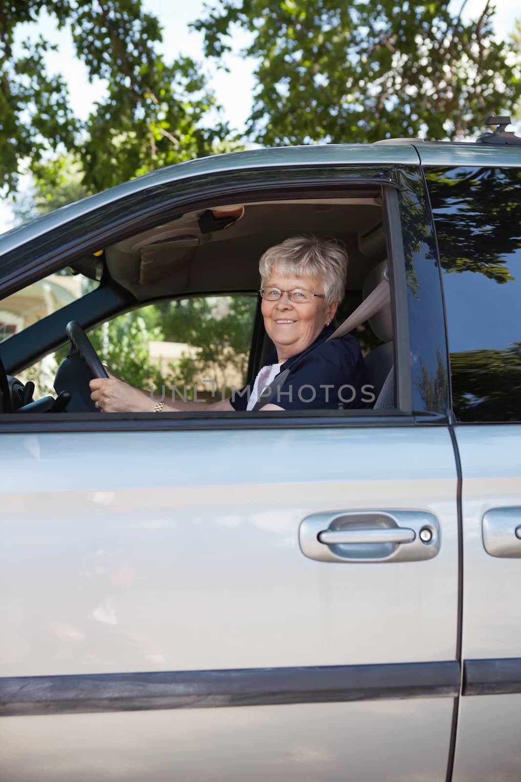 Pretty senior woman driving car by leaf