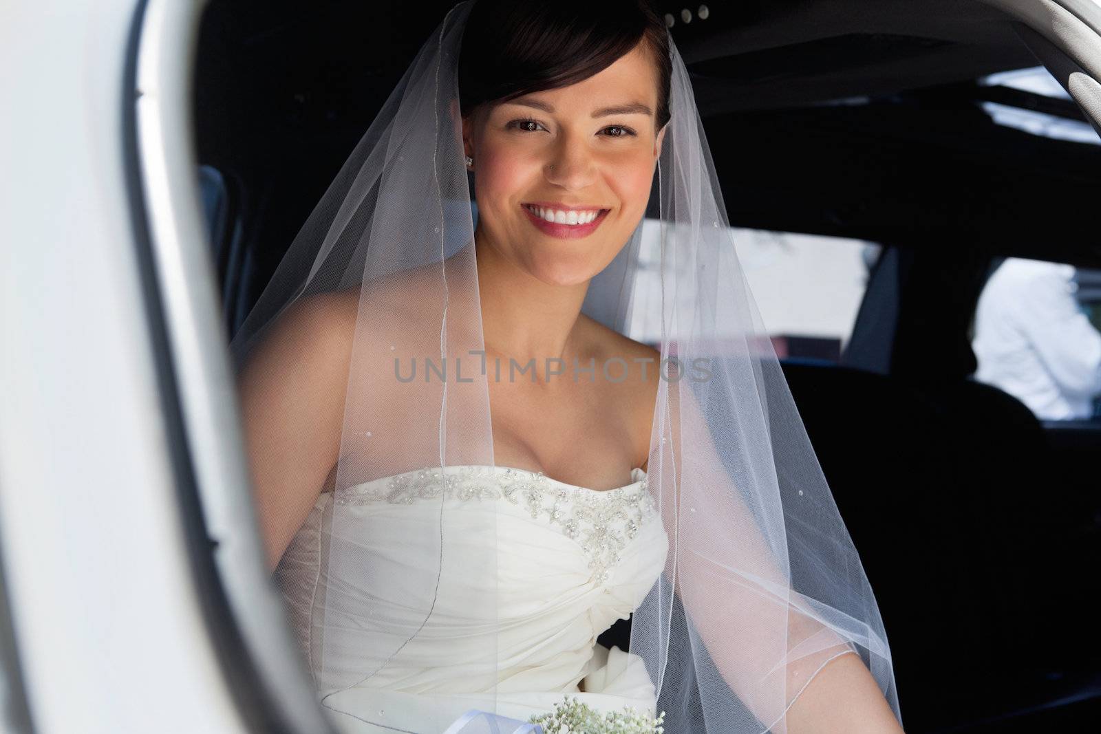 Attractive bride sitting in car and smiling