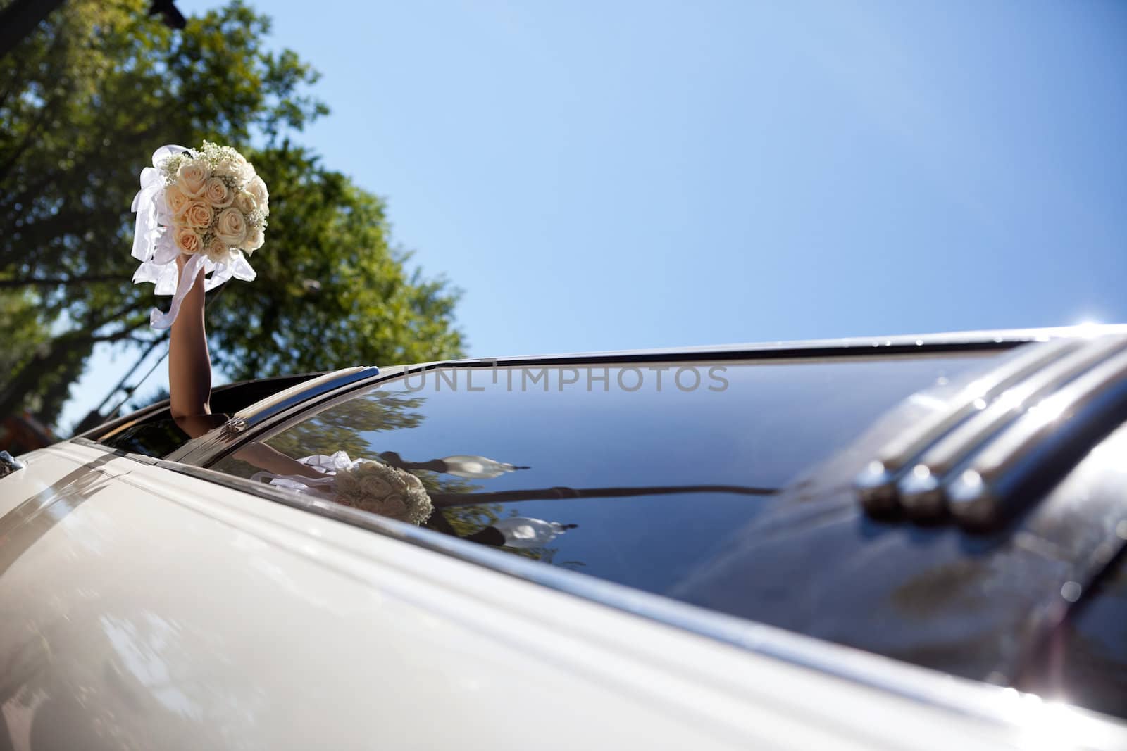 Bride waving hand from limousine holding flower bouquet