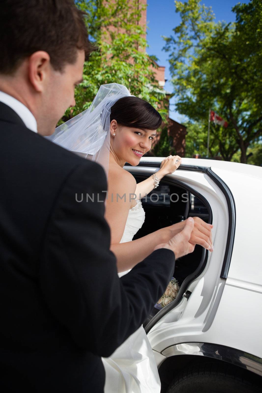 Groom helping bride into limousine