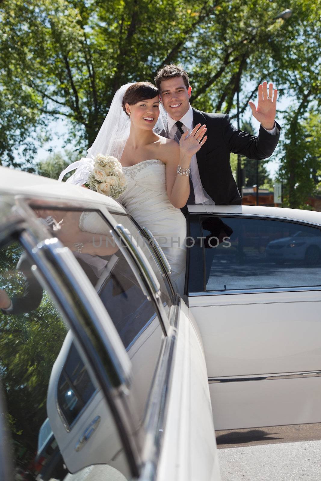 Bride and groom standing in Limo waving