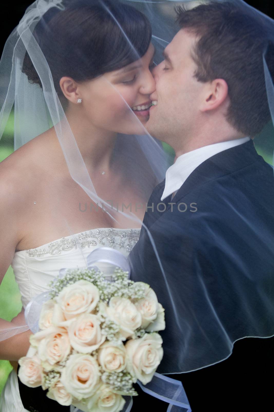 Newlywed Couple Kissing Each Other Holding Flower Bouquet In Hand.