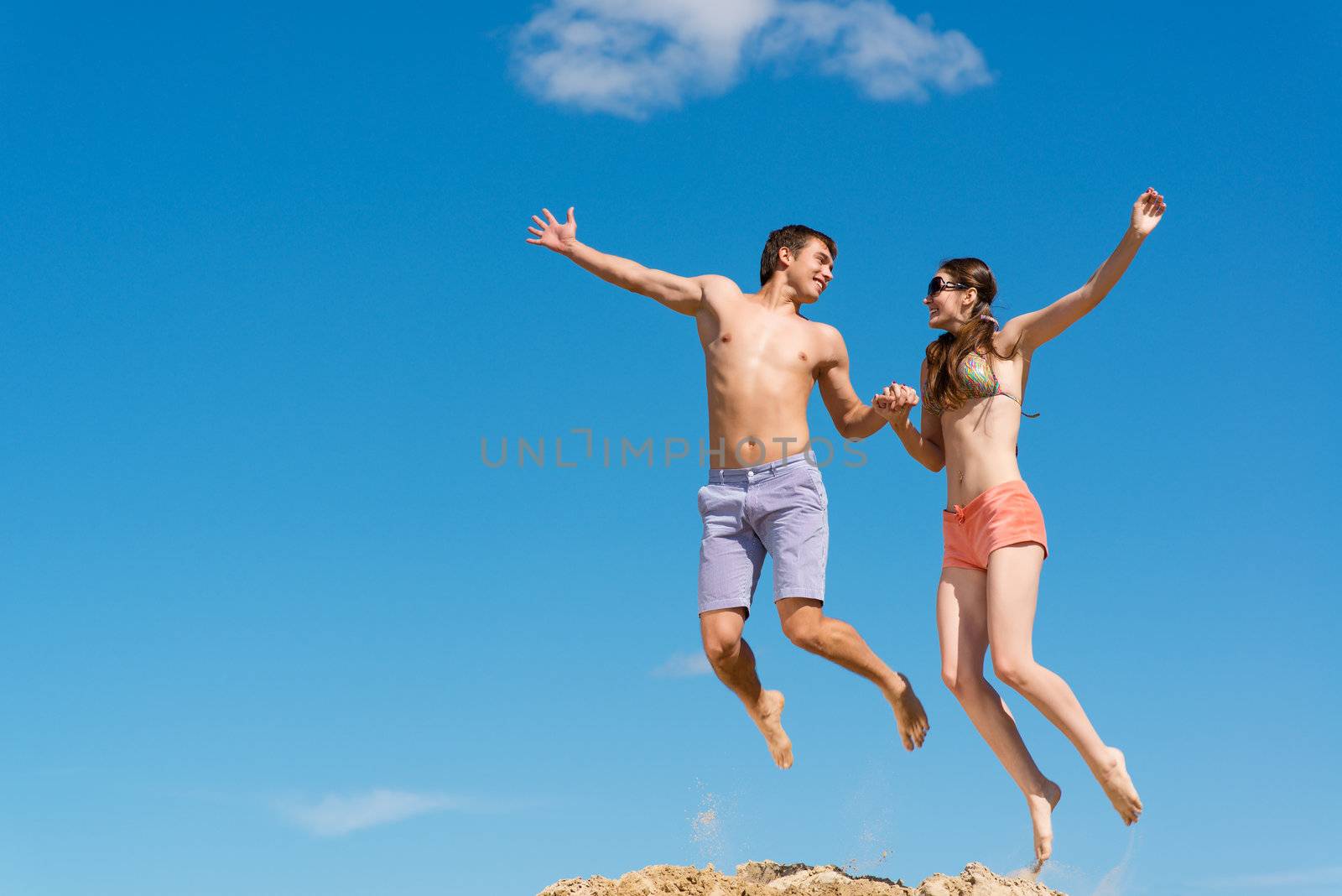 couple jumping together holding hands on a background of blue sky