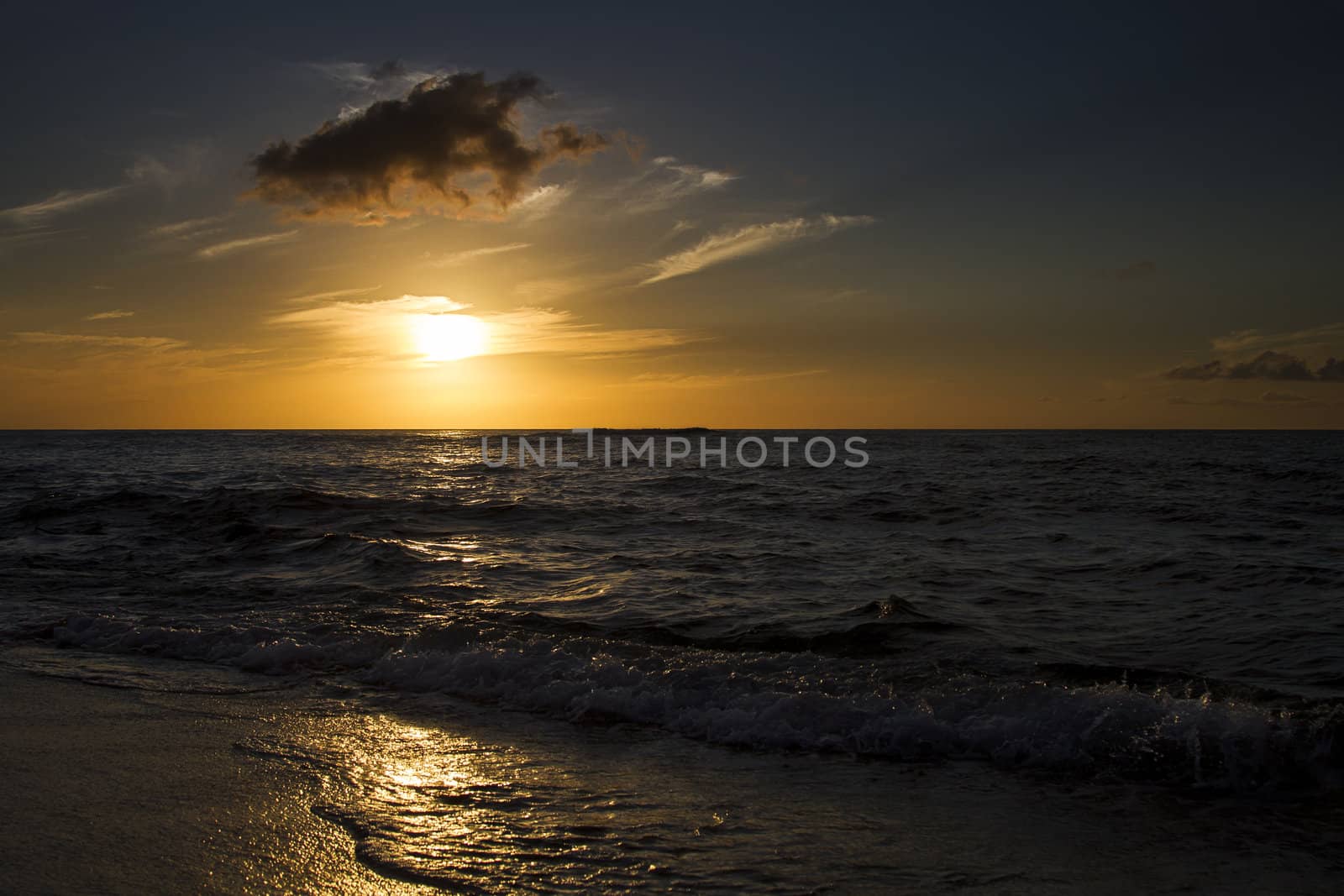Sunset over a calm pacific ocean on a beach being pounded by waves