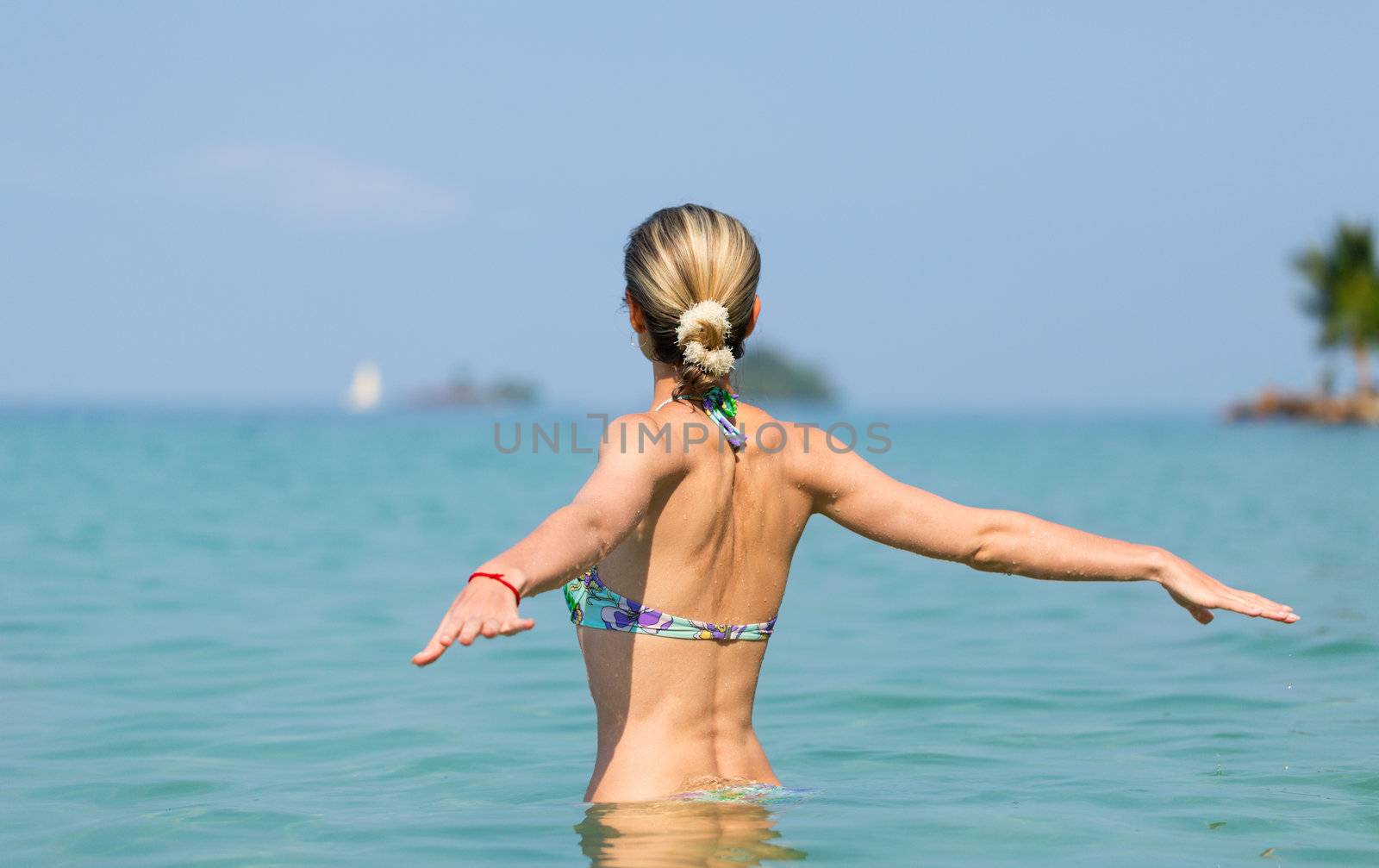 Beautiful young slim girl in the water in the sea, looking away. With his back to the camera.