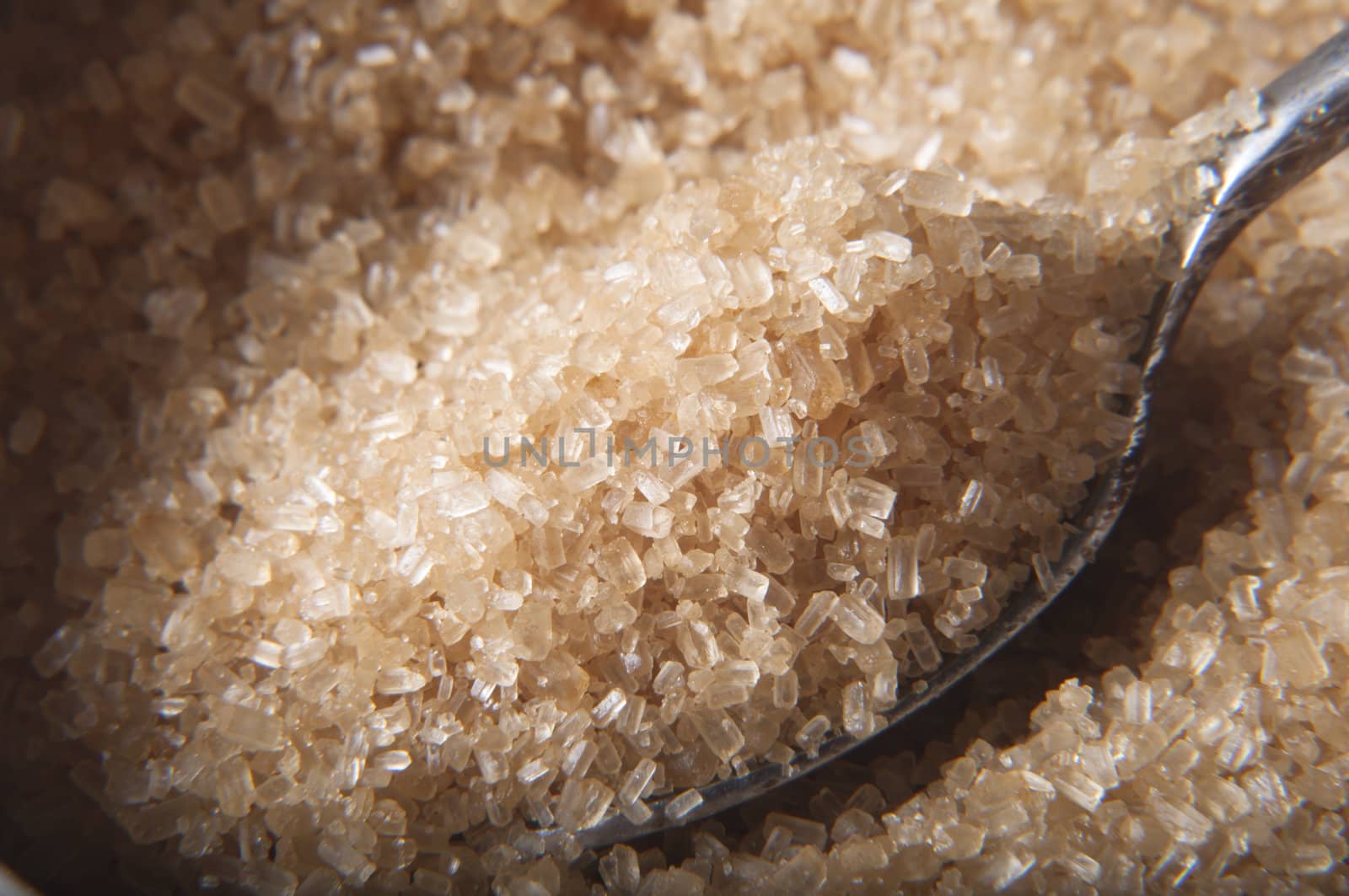 Close up (macro) shot.  A spoon filled with brown raw cane (demerera) sugar granules being lifted from bowl.  Selective focus.