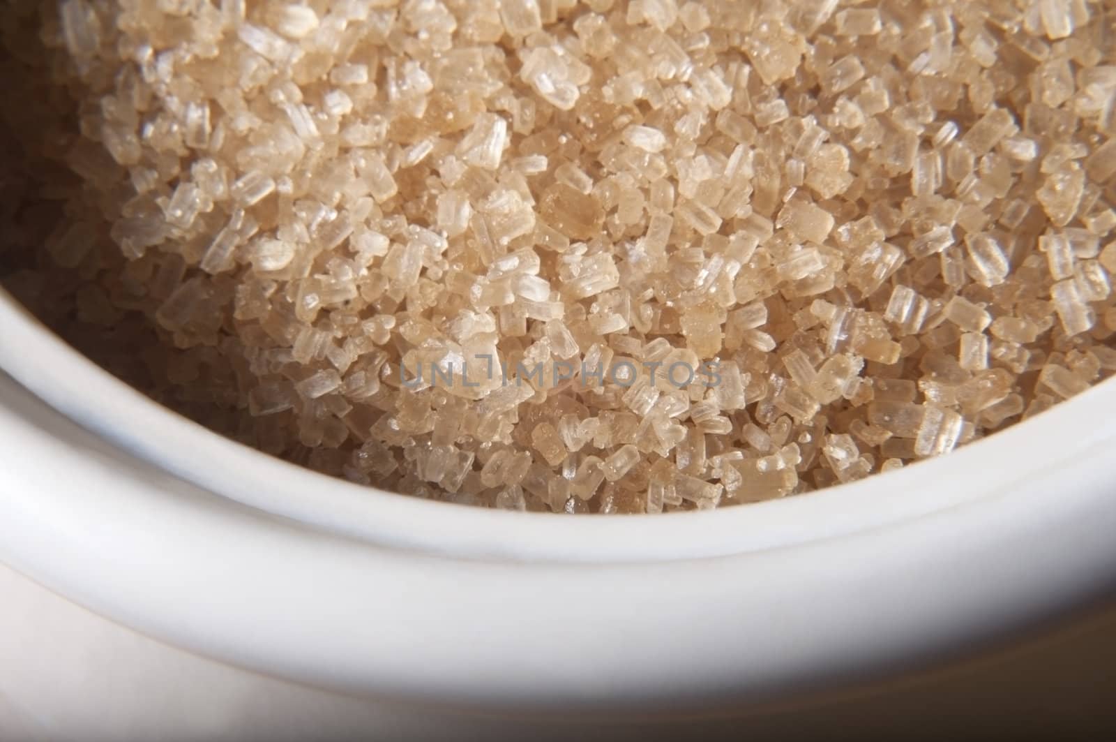 Close up (macro) of granulated brown sugar (demerera) in a cream coloured china bowl.