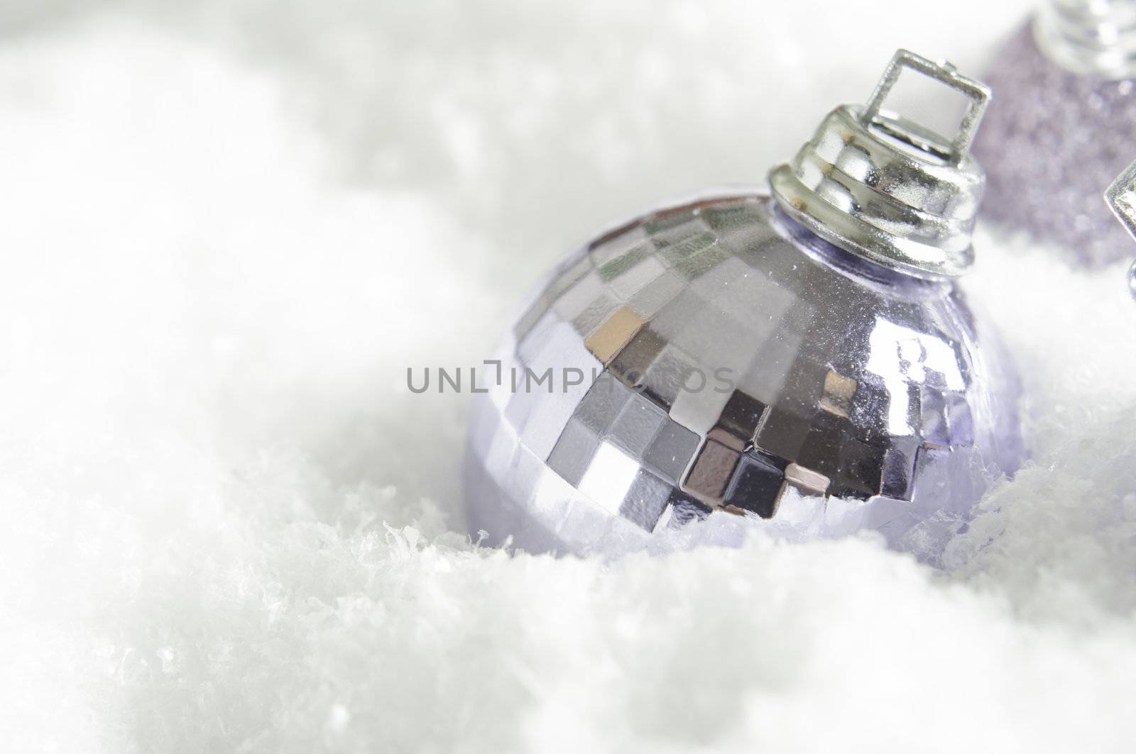 A lilac (light purple) Christmas bauble partly submerged in fake snow.  Snowy surface provides copy space to left and beneath the ornament.