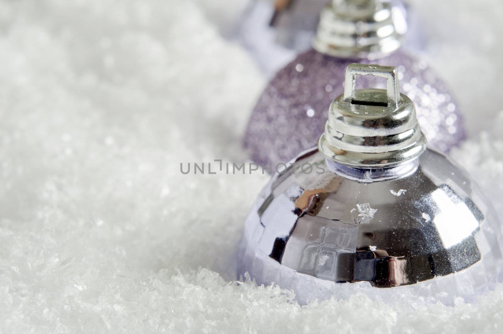 Three Christmas baubles - alternately faceted and sparkling, sinking into fake snow and positioned in a line leading away from the viewer.   Copy space on left side.