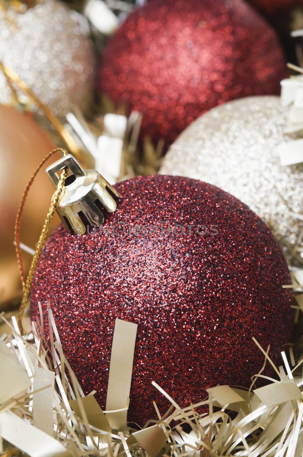 Close up of Christmas baubles and gold tinsel garland.  Red, sparkling bauble in foreground.  Portrait (vertical) orientation.  Shallow depth of field.