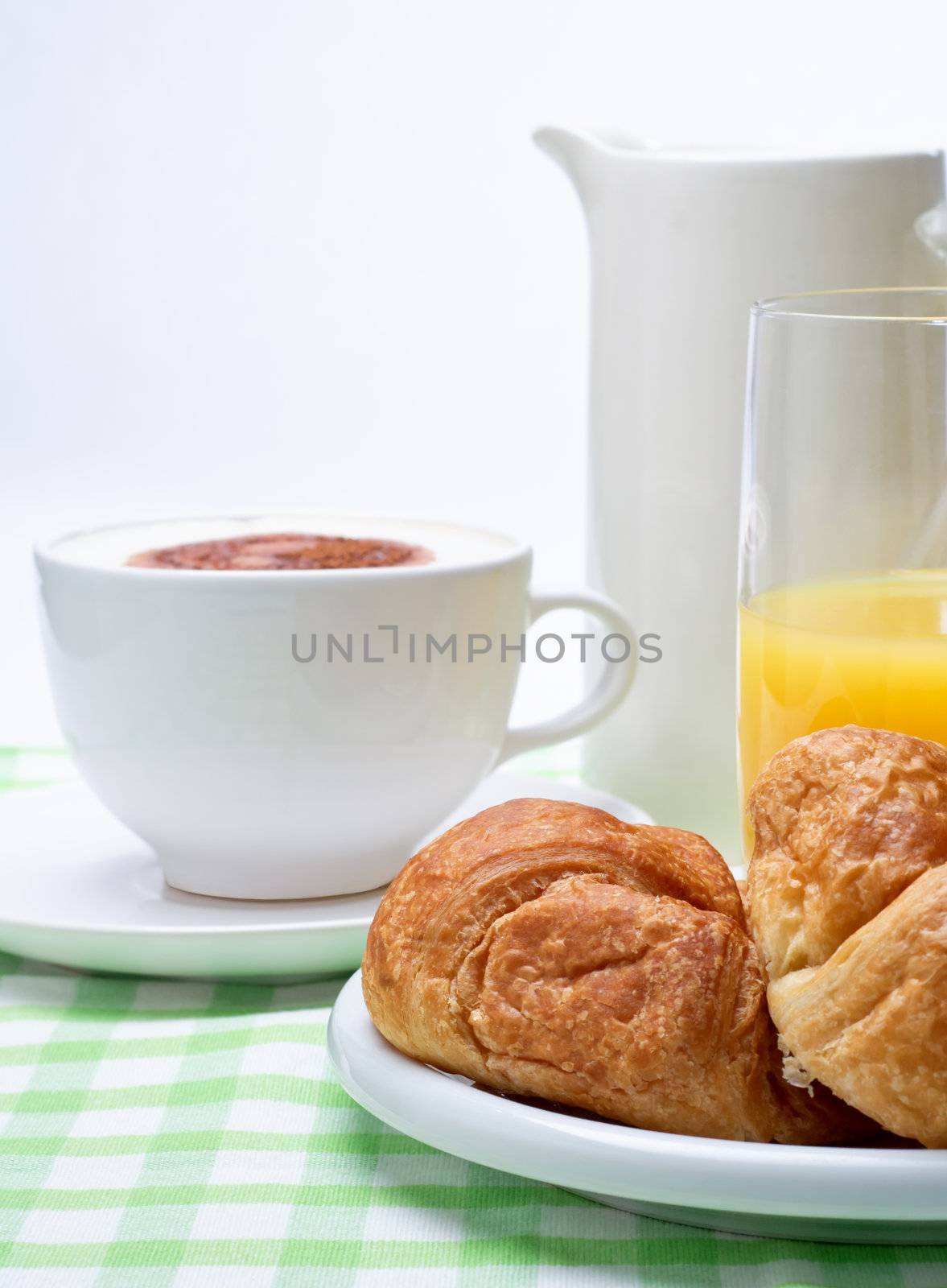 A breakfast setting  of croissant, orange juice and coffee on a green gingham table cloth.  