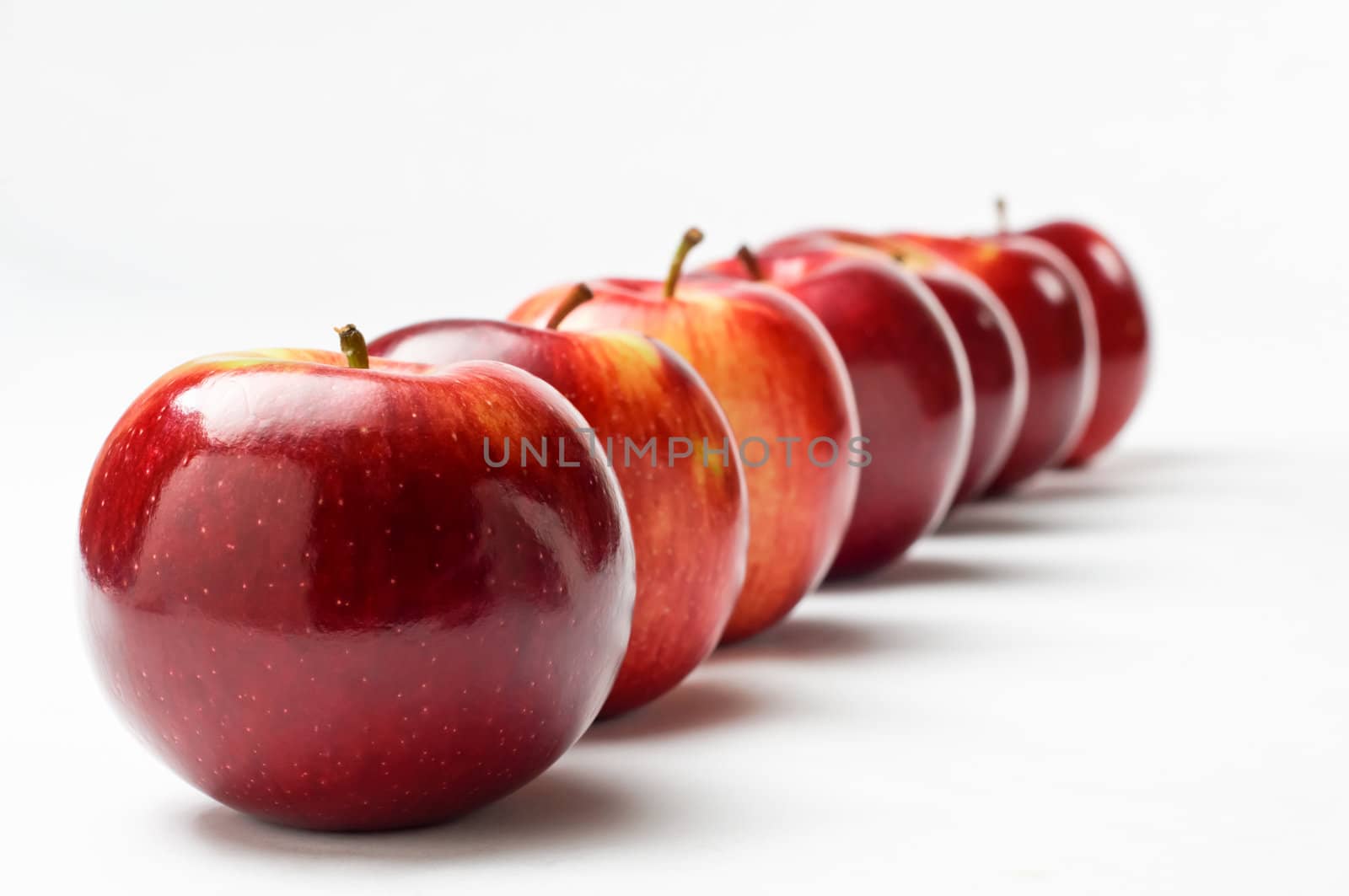 Close up of a row of seven shiny red apples leading away from the viewer at an oblique apple.