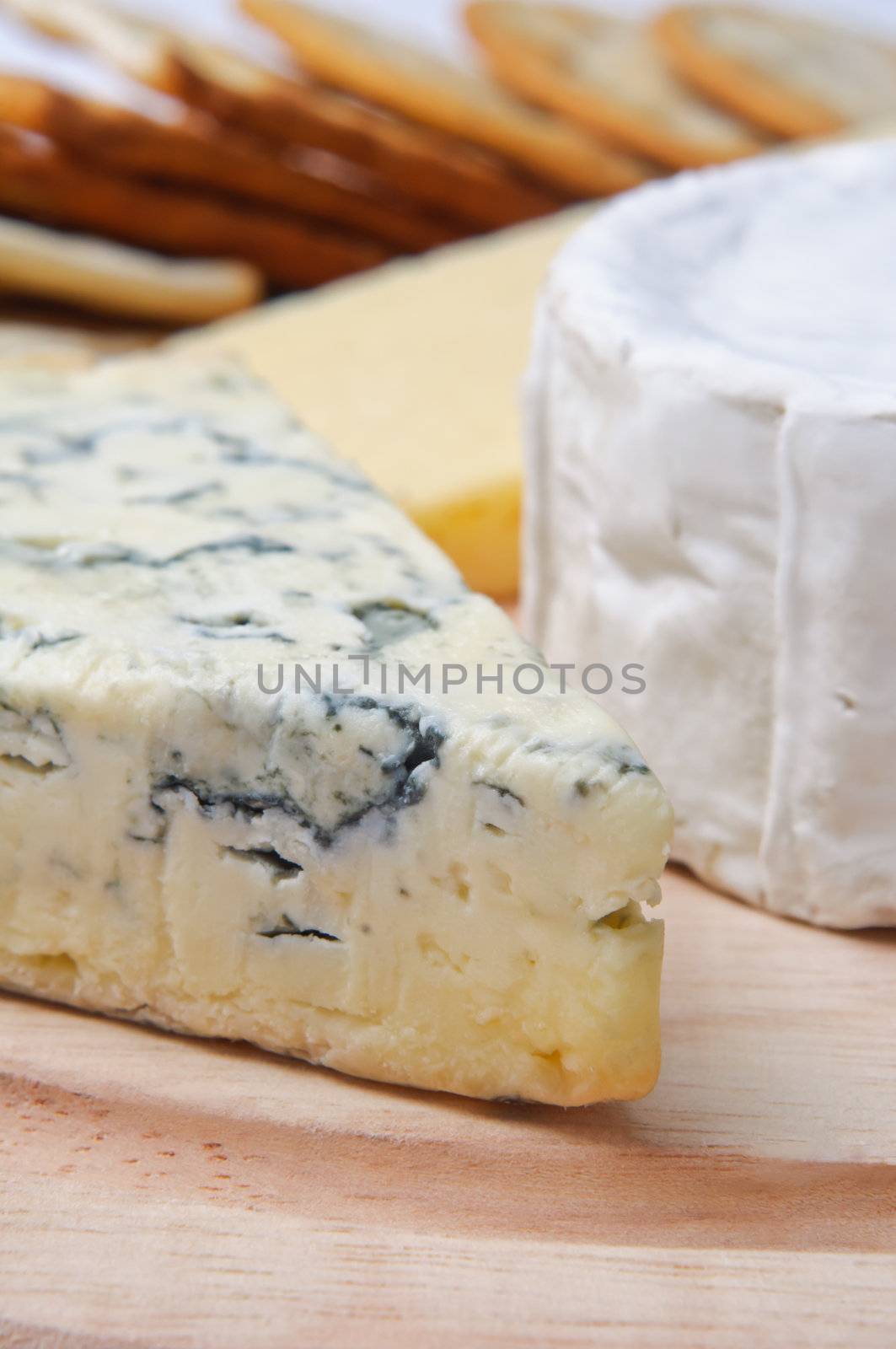 Close up of cheese selection on wooden board with crackers in soft focus background.  Focus is on French blue veined cheese.