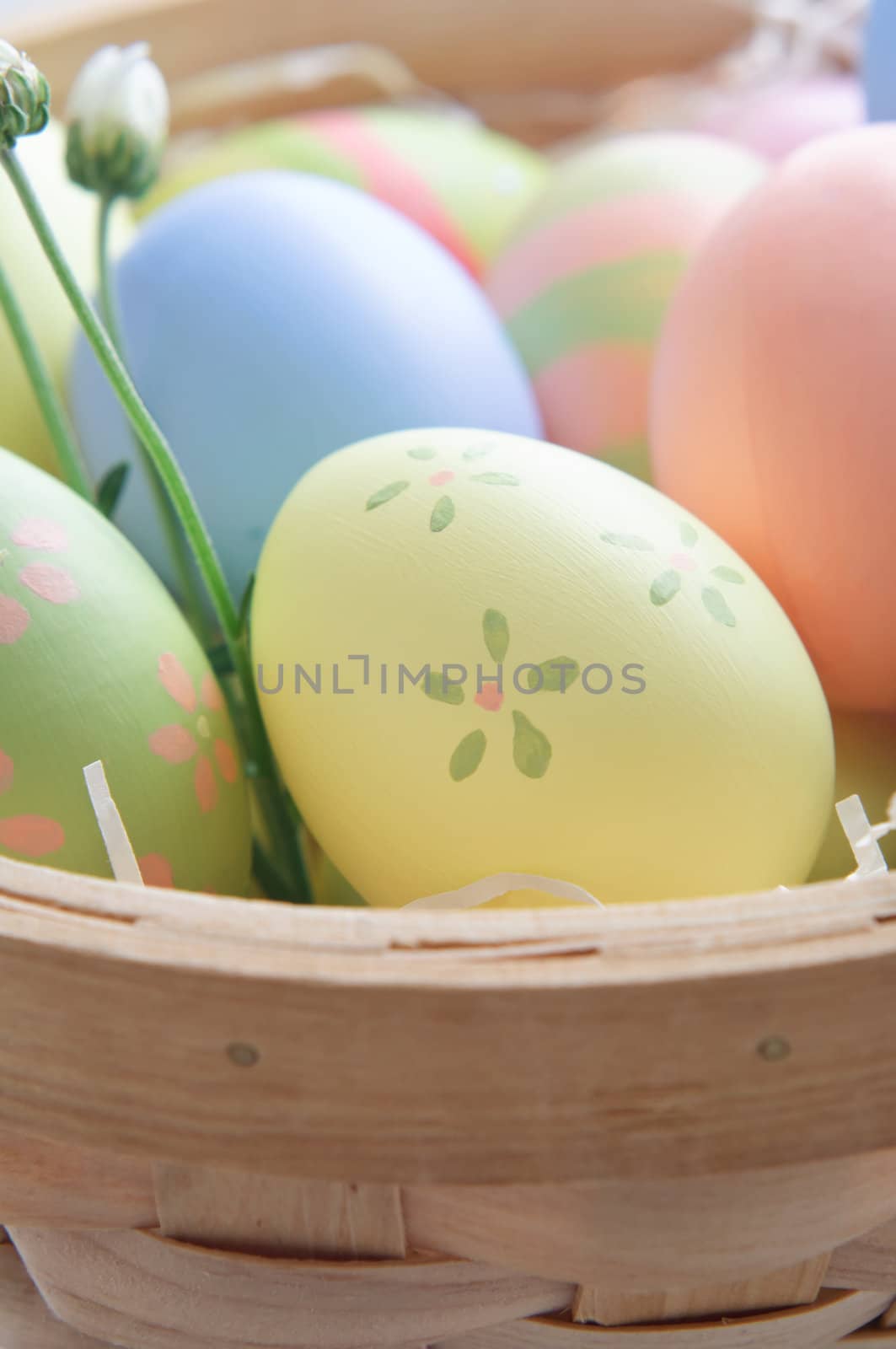 Close up of decorated Easter eggs (hand painted by the photographer) in a woven wooden basket with paper straw and budding flowers.  Shallow depth of field.