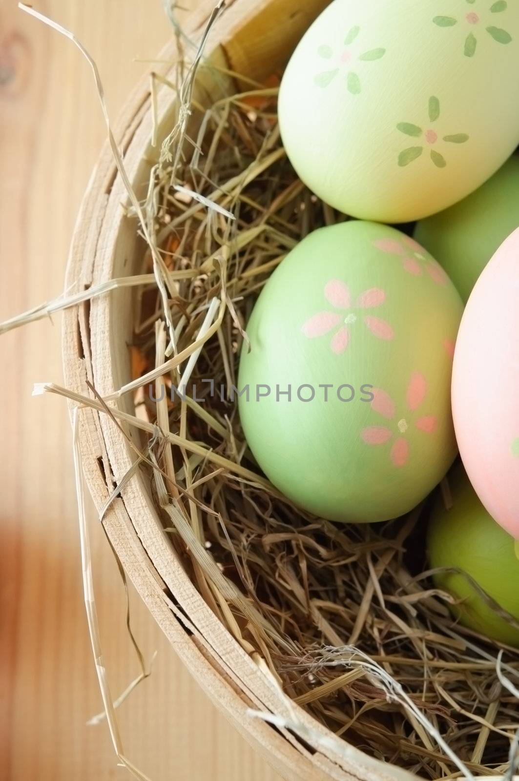 Overhead close up shot of hand painted Easter eggs nestling in straw in a basket on a wooden table.  Portrait orientation.