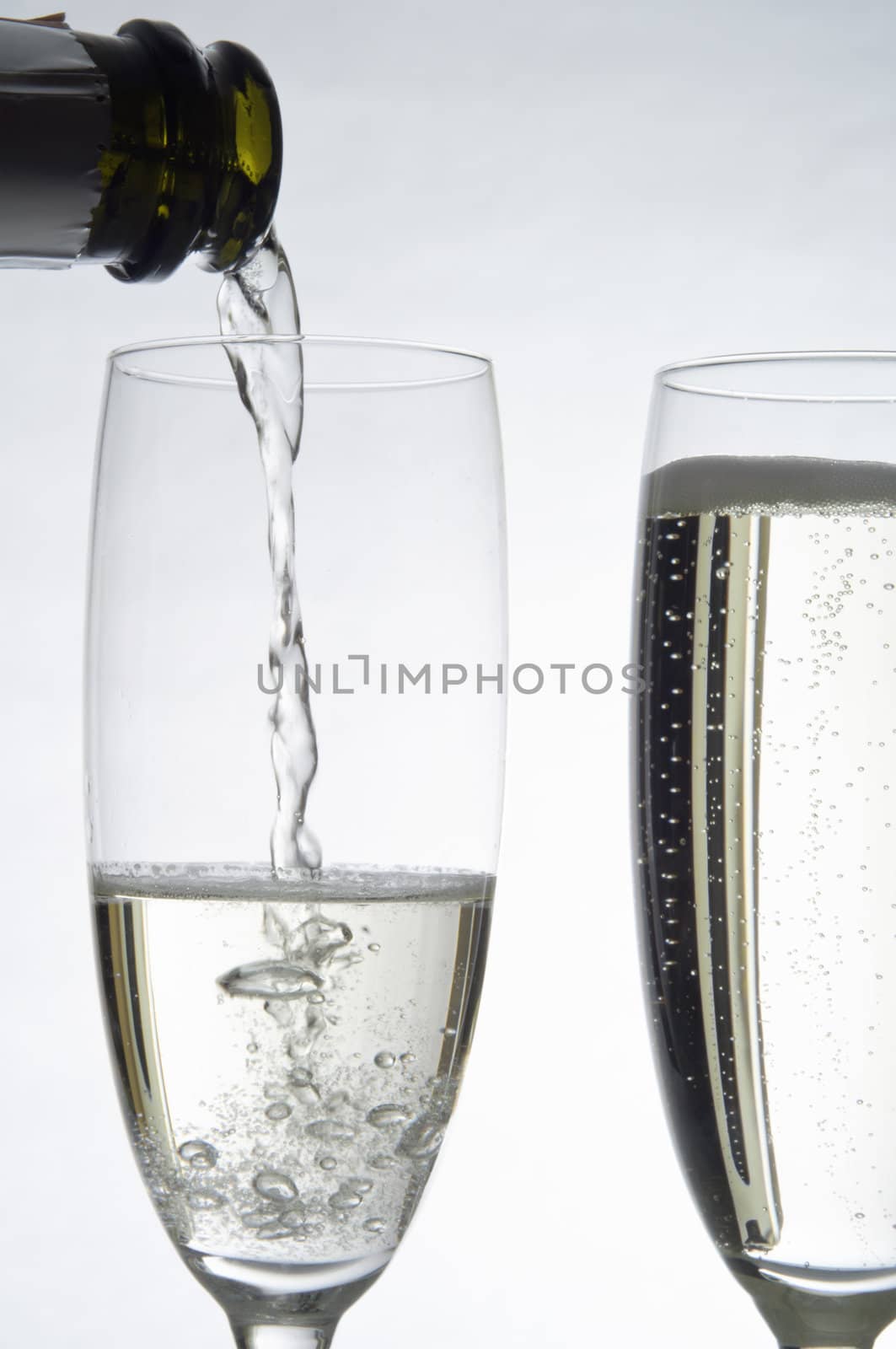 Action shot of a stream of Champagne pouring from a bottle into a fluted glass.  A second glass on the right is already filled.