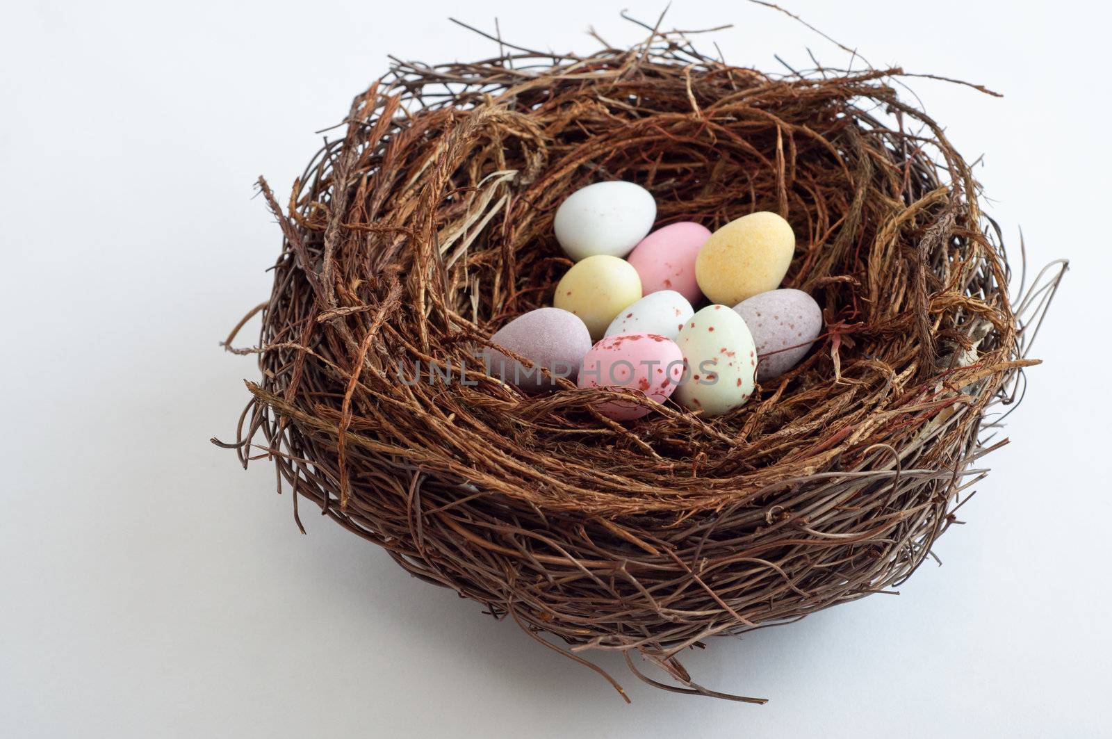 Whole object shot of colourful Easter egg sweets in a woven twig bird's nest.