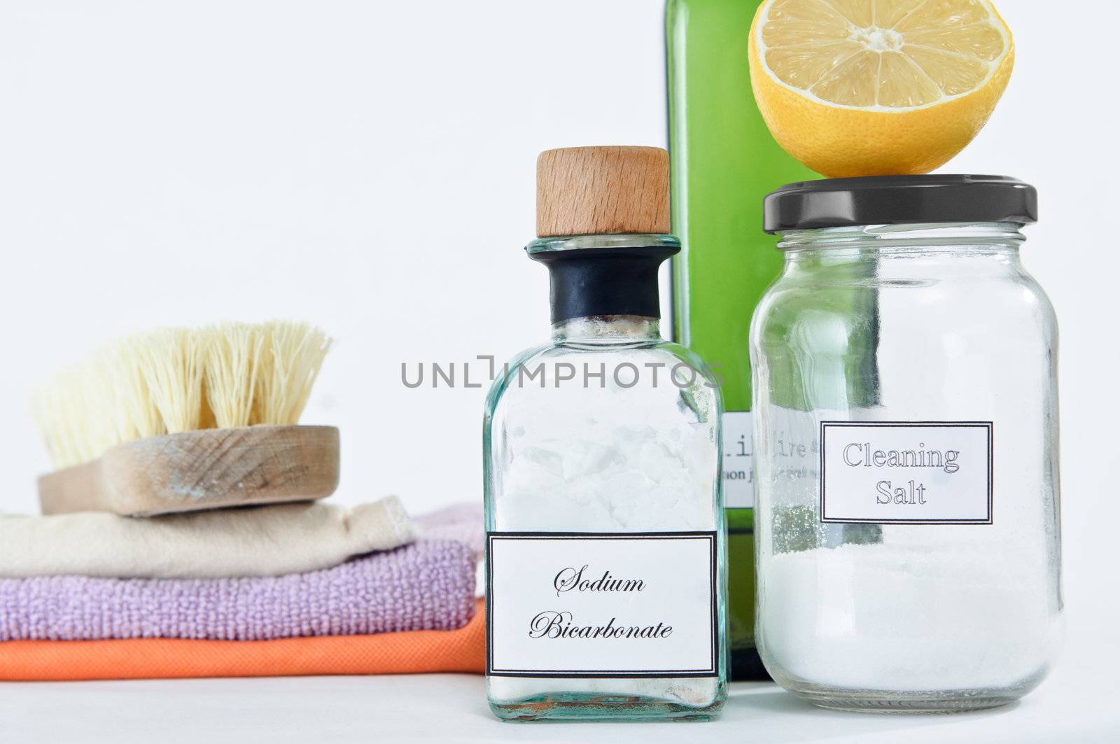 A range of non-toxic cleaning products in glass jars and bottles with a stack of cleaning cloths and scrubbing brush.  Copy space upper left.