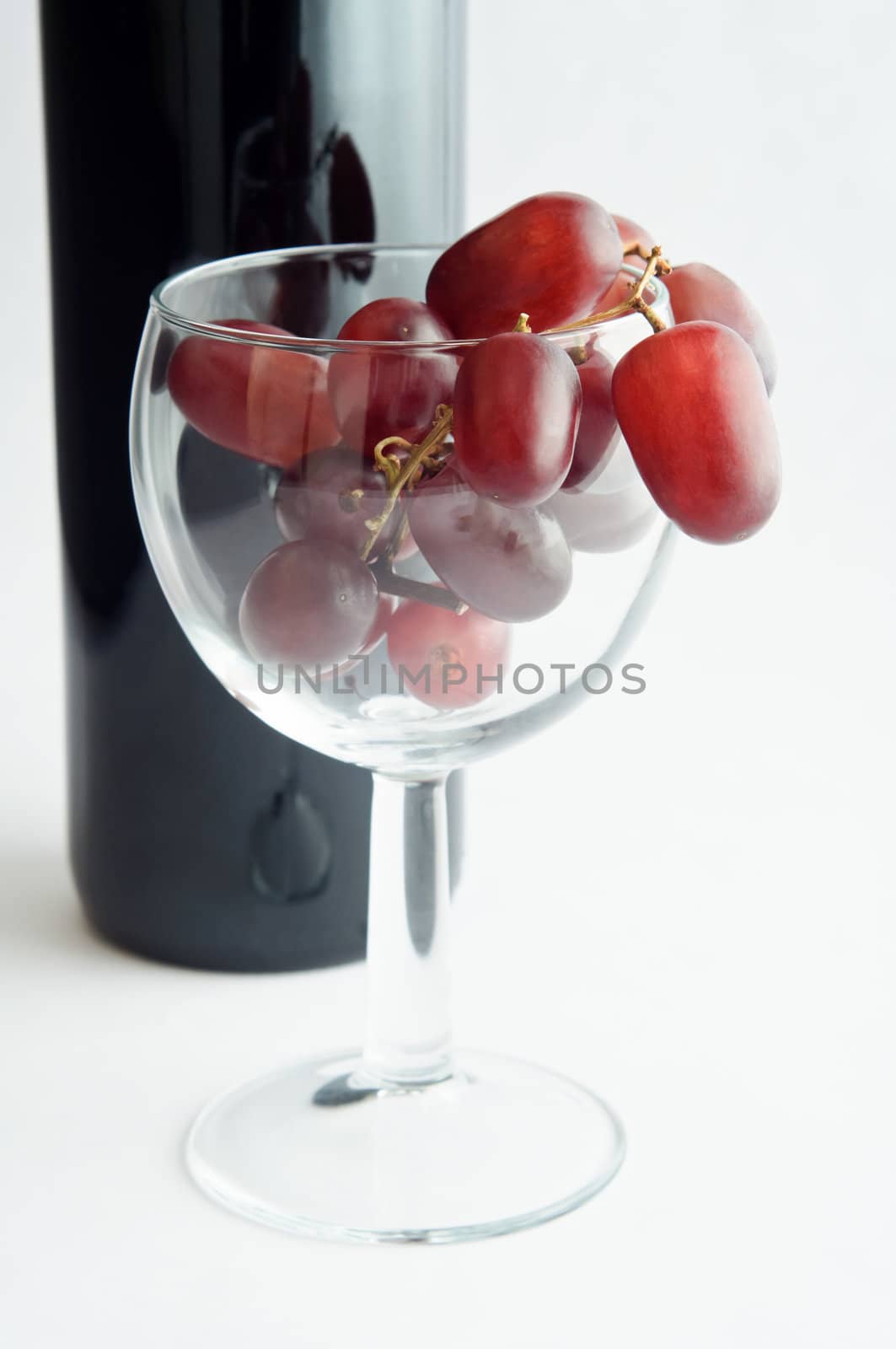 A wine glass filled with red grapes in front of a bottle of red wine.  Portrait (vertical) orientation.