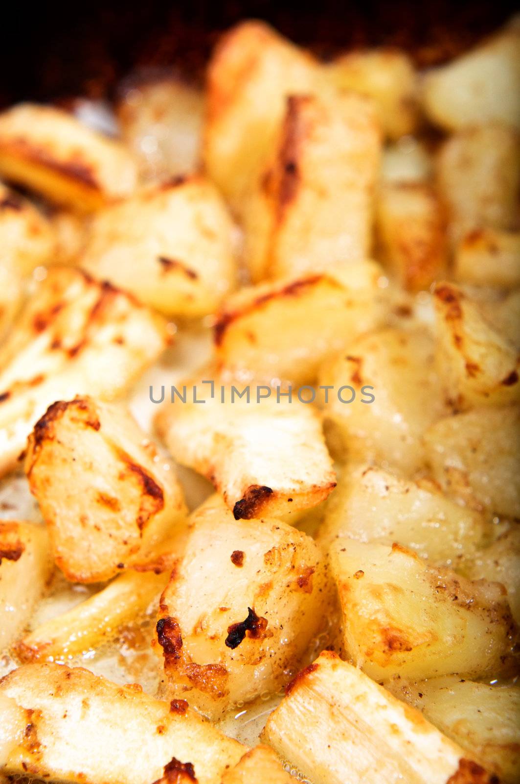 Crispy roast potatoes and parsnips in hot, bubbling oil.  Vertical (portrait) orientation.