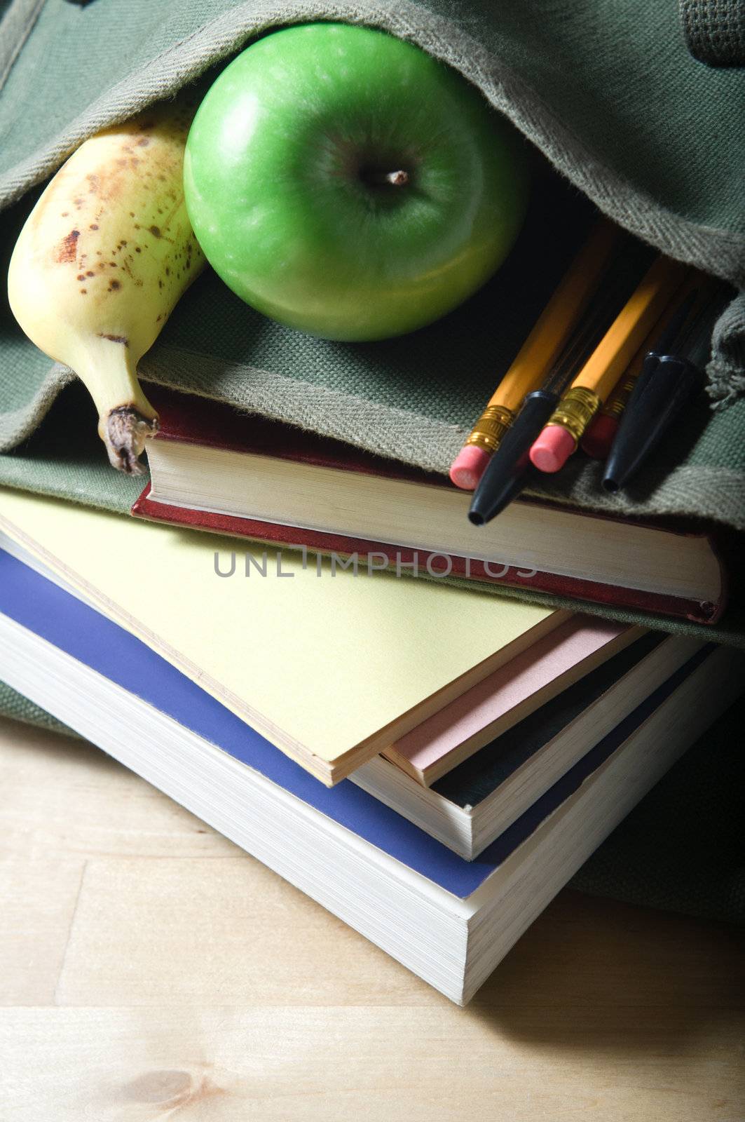 An open school satchel, containing books, pens, pencils and fruit.  Vertical (portrait) orientation.