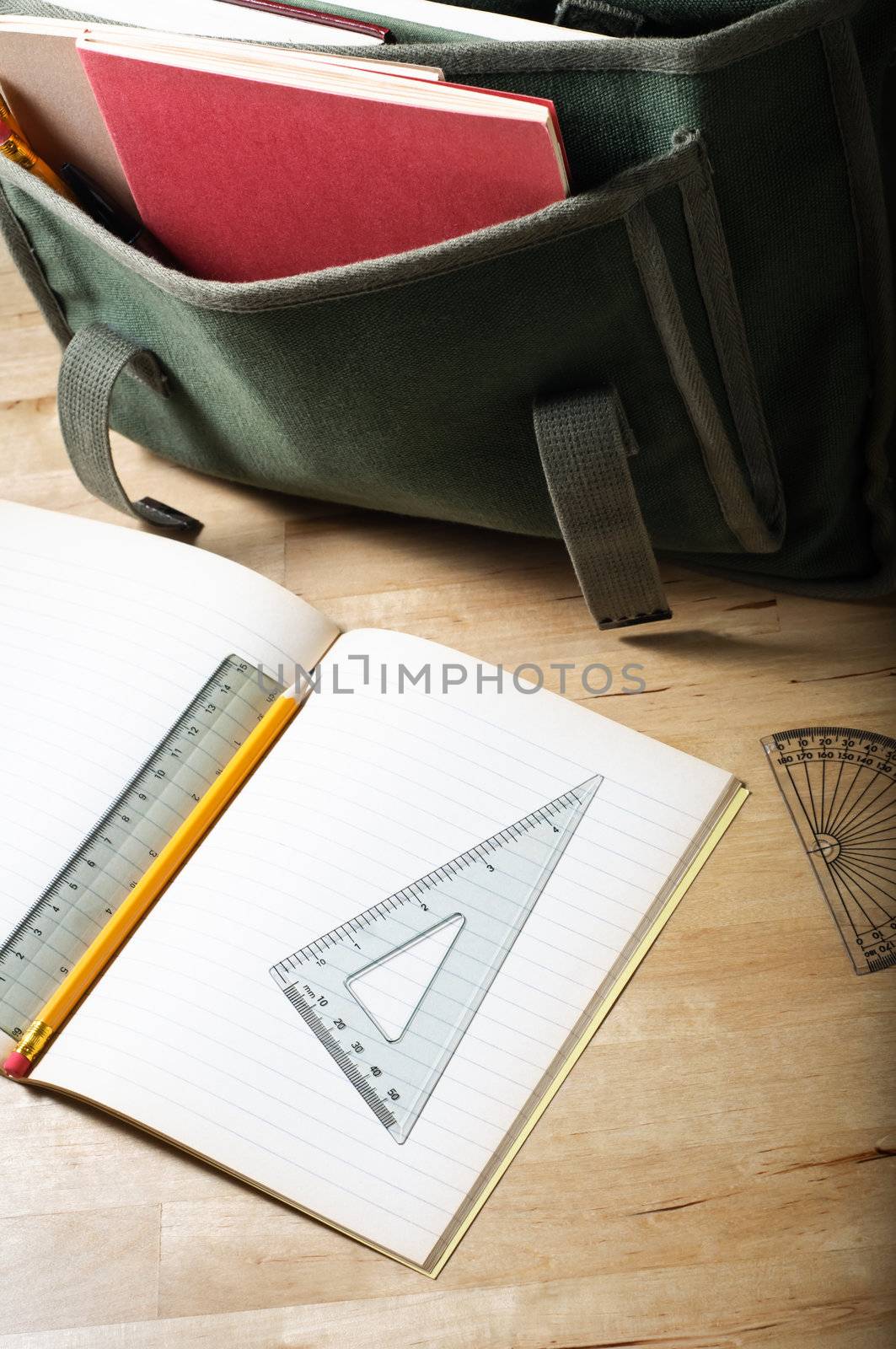 A school satchel on a wooden table, behind an open exercise book with maths equipment.